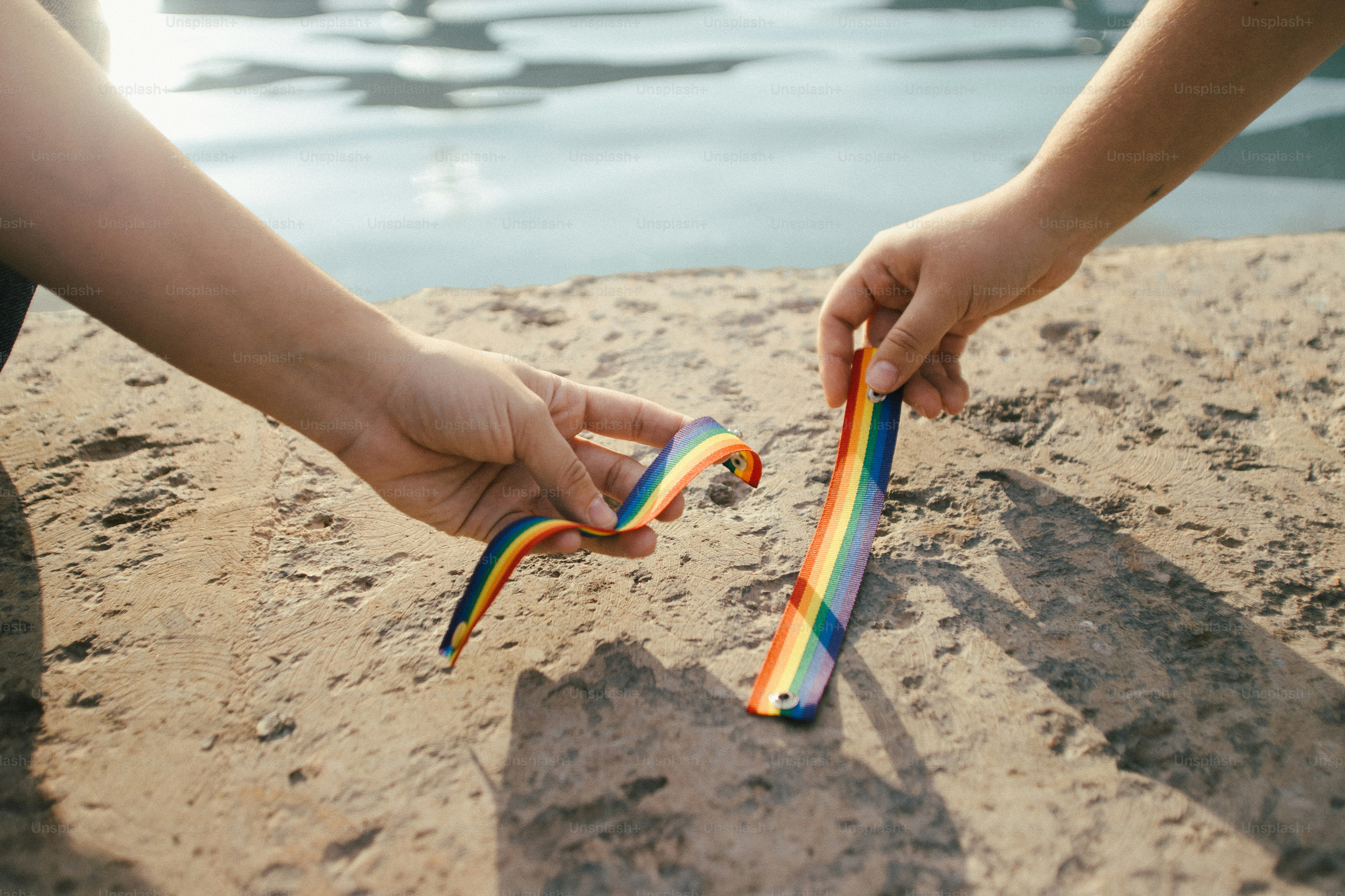 Deux mains tenant des objets rayés arc-en-ciel sur le sable