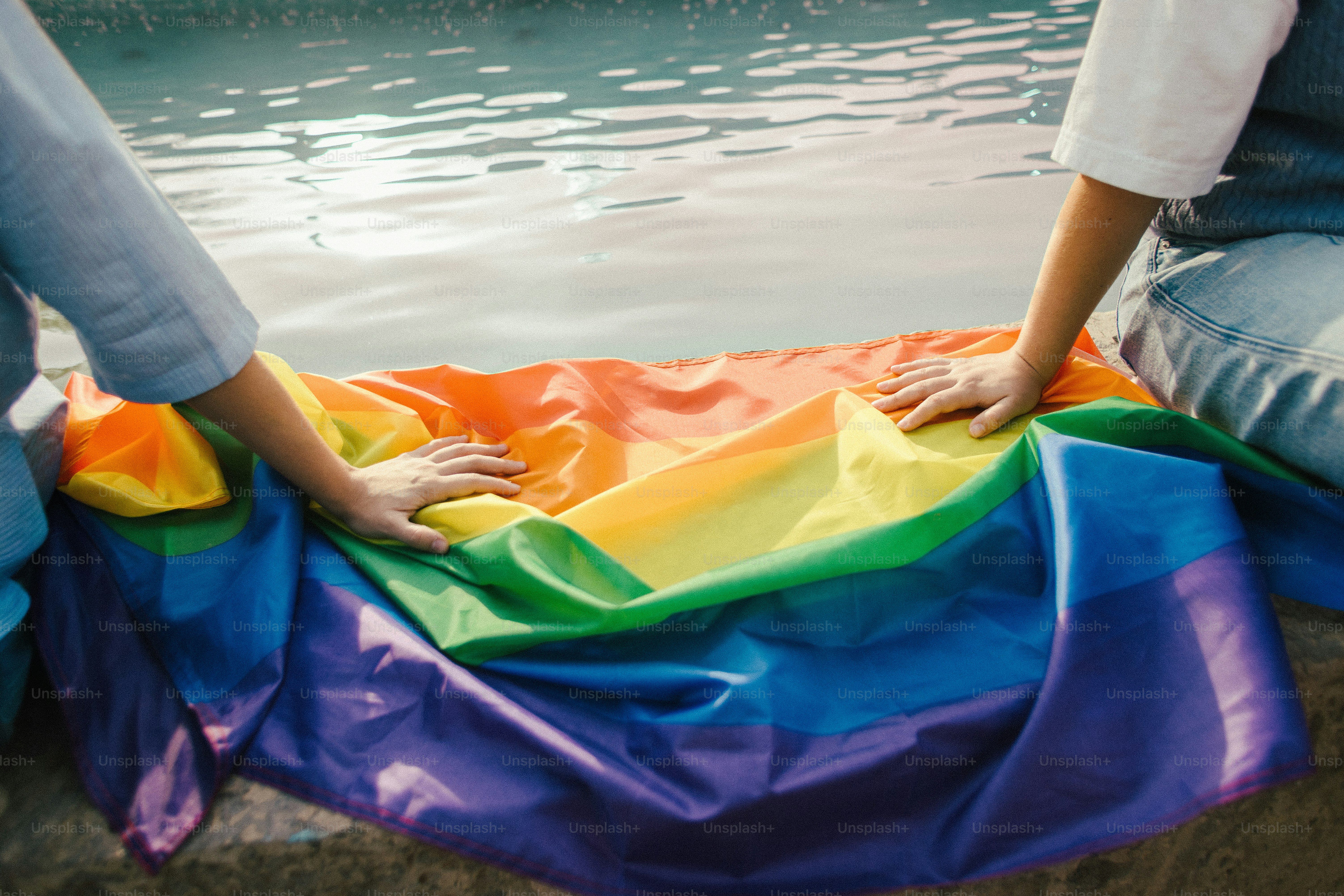 Deux personnes tiennent un drapeau arc-en-ciel au bord de l’eau