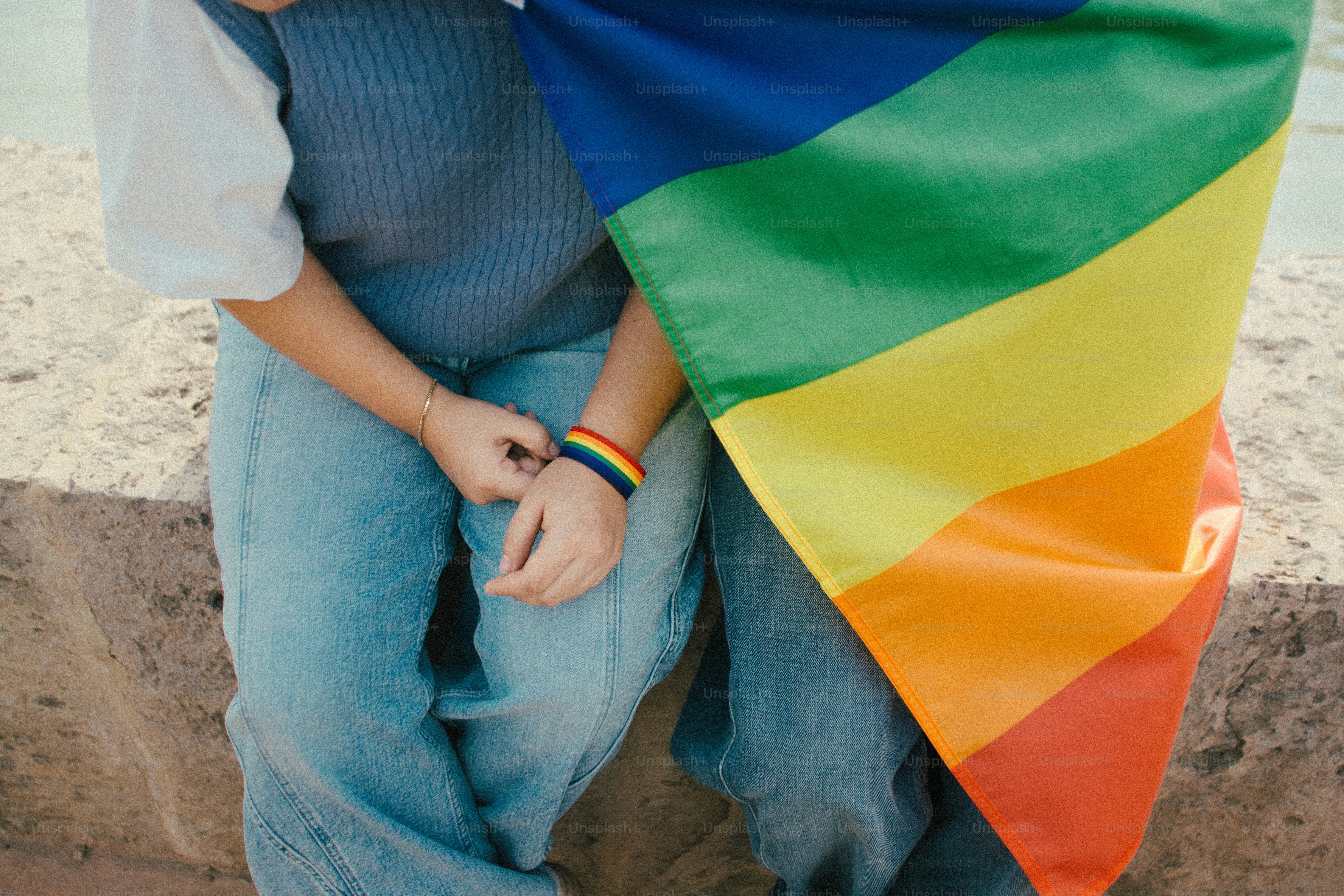 Deux personnes se tenant la main sous un drapeau arc-en-ciel.