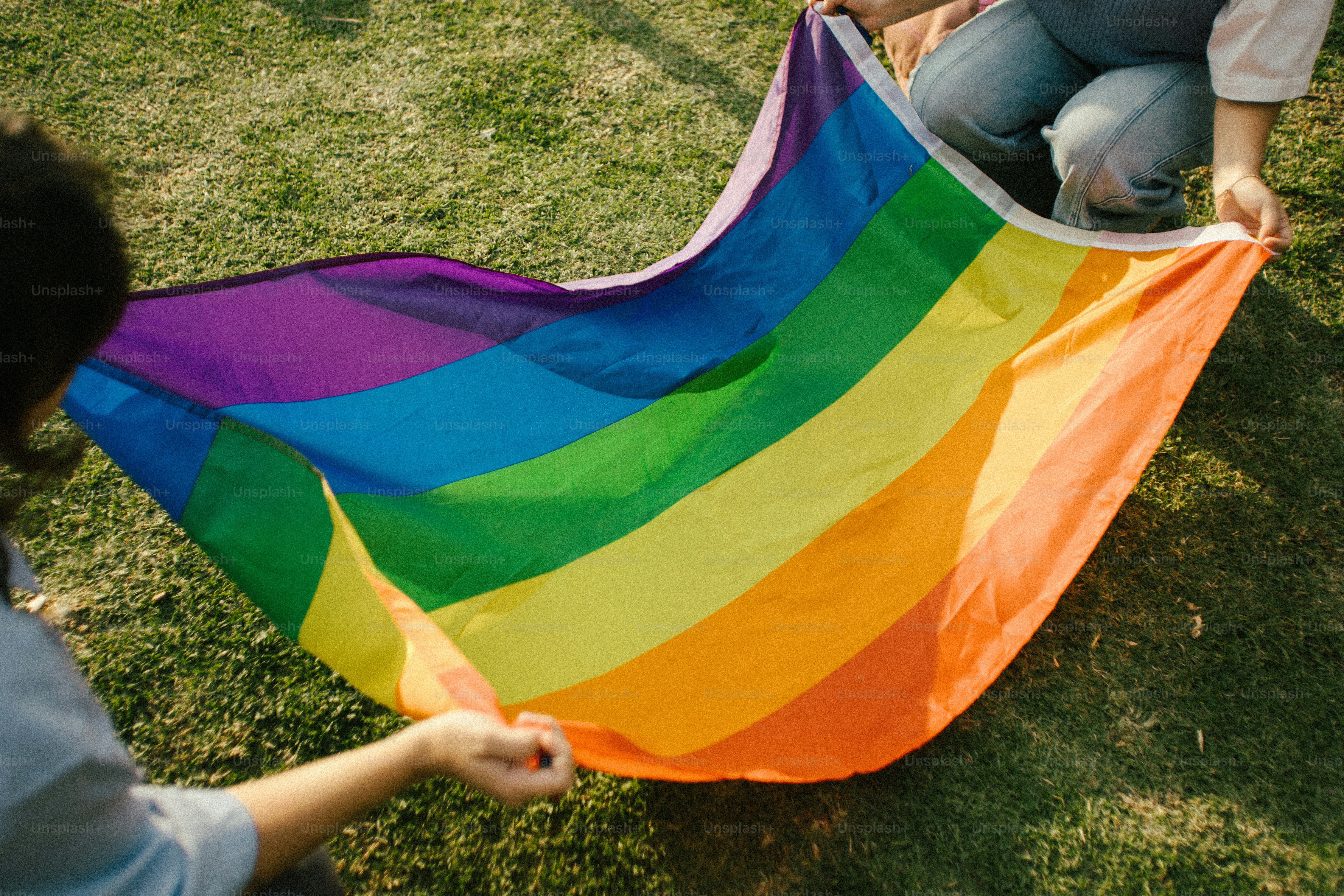 Deux personnes tenant un drapeau arc-en-ciel sur l’herbe
