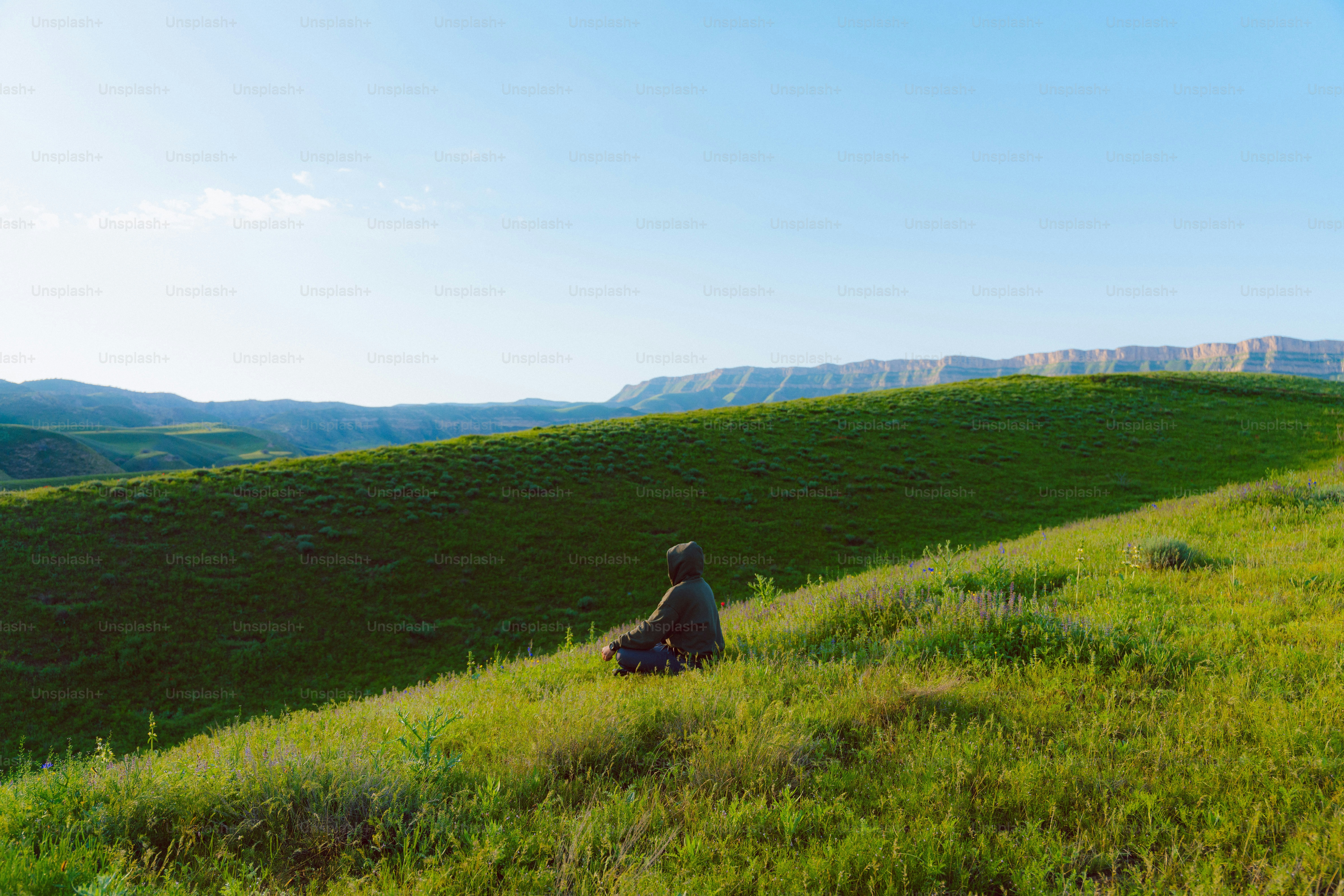Pessoa sentada em uma colina gramada sob um céu limpo.