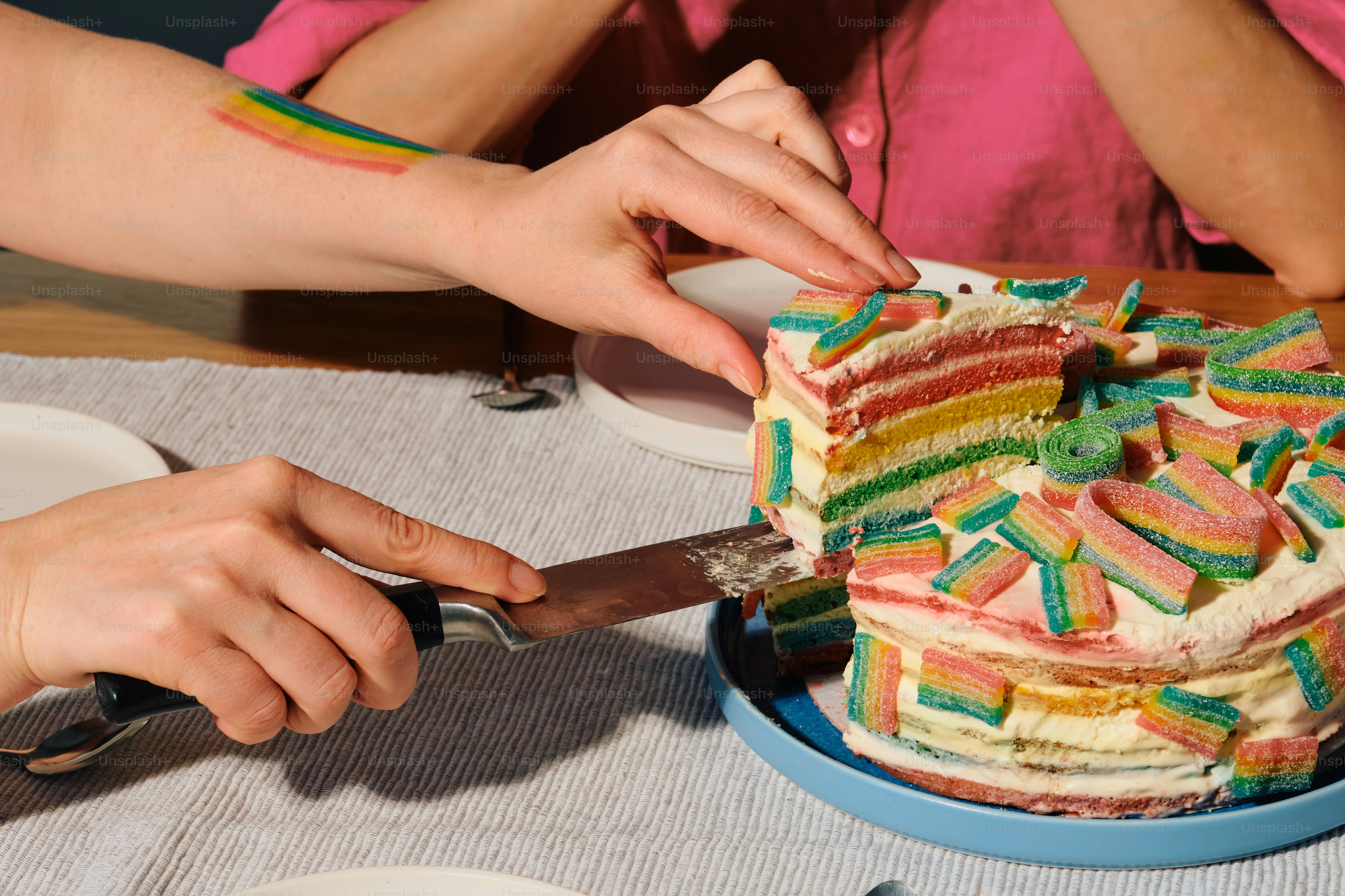 Mani che tagliano una colorata torta arcobaleno con decorazioni di caramelle