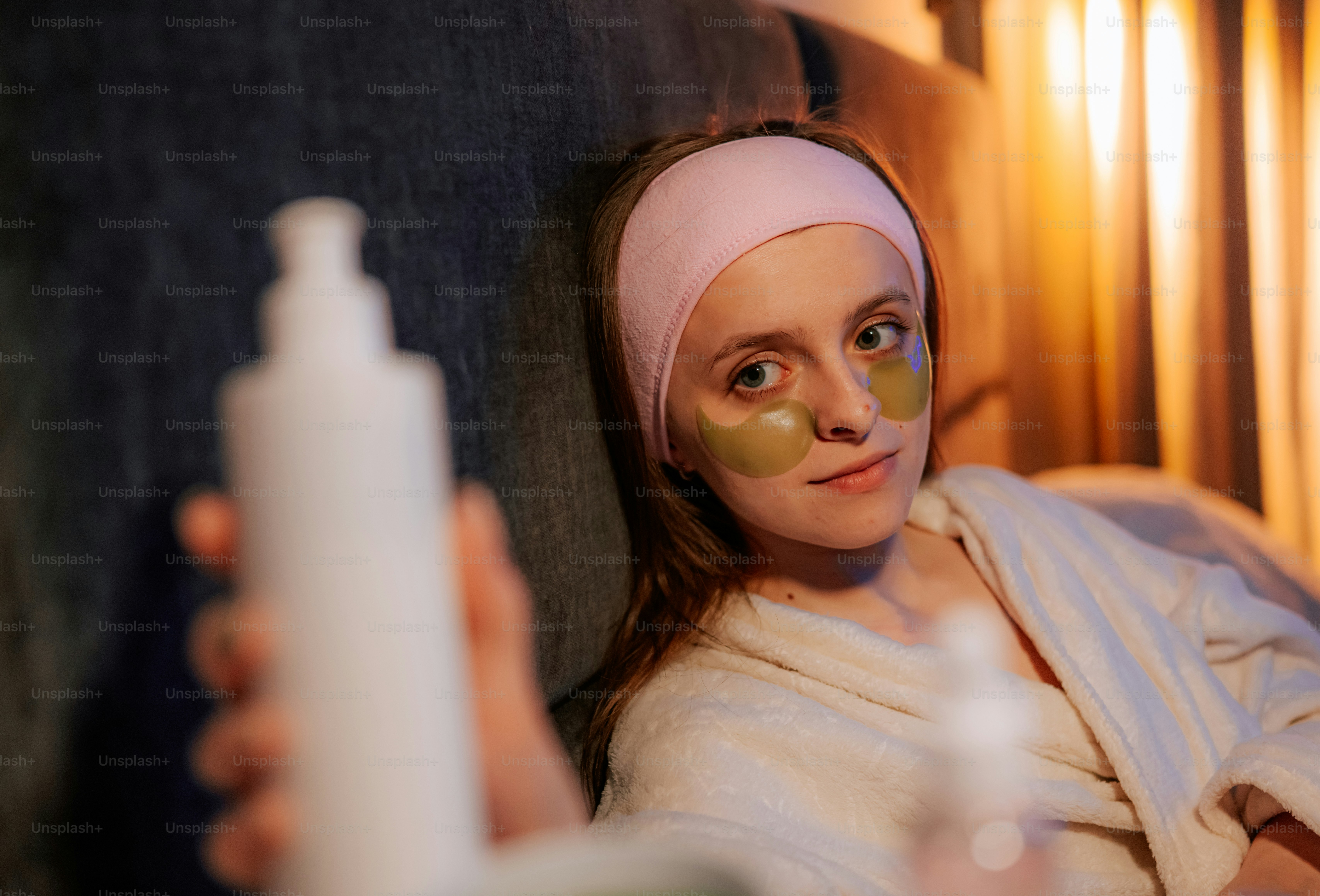 Woman with eye patches and headband holds a beauty product