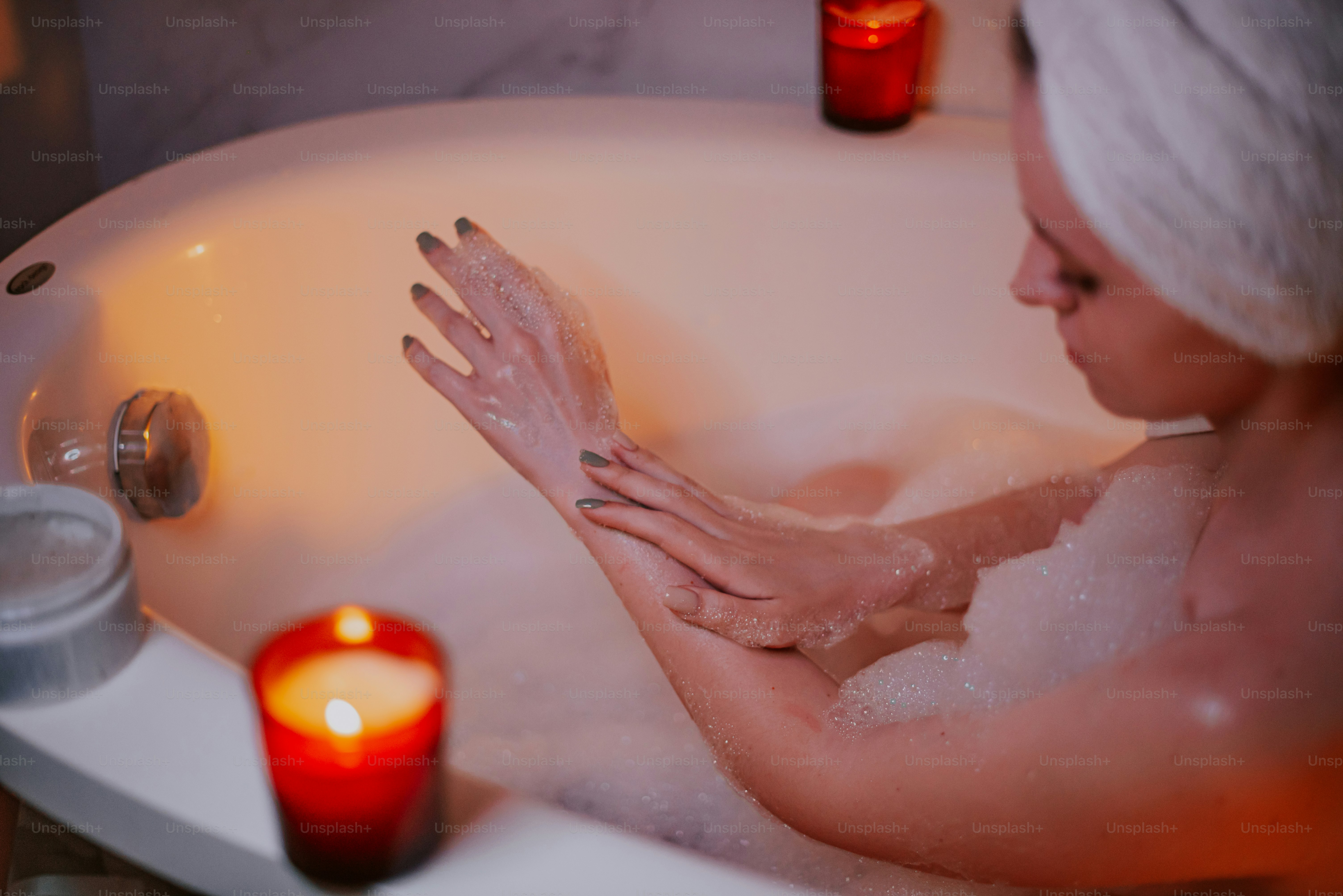 Woman applying lotion in a bubble bath with candles