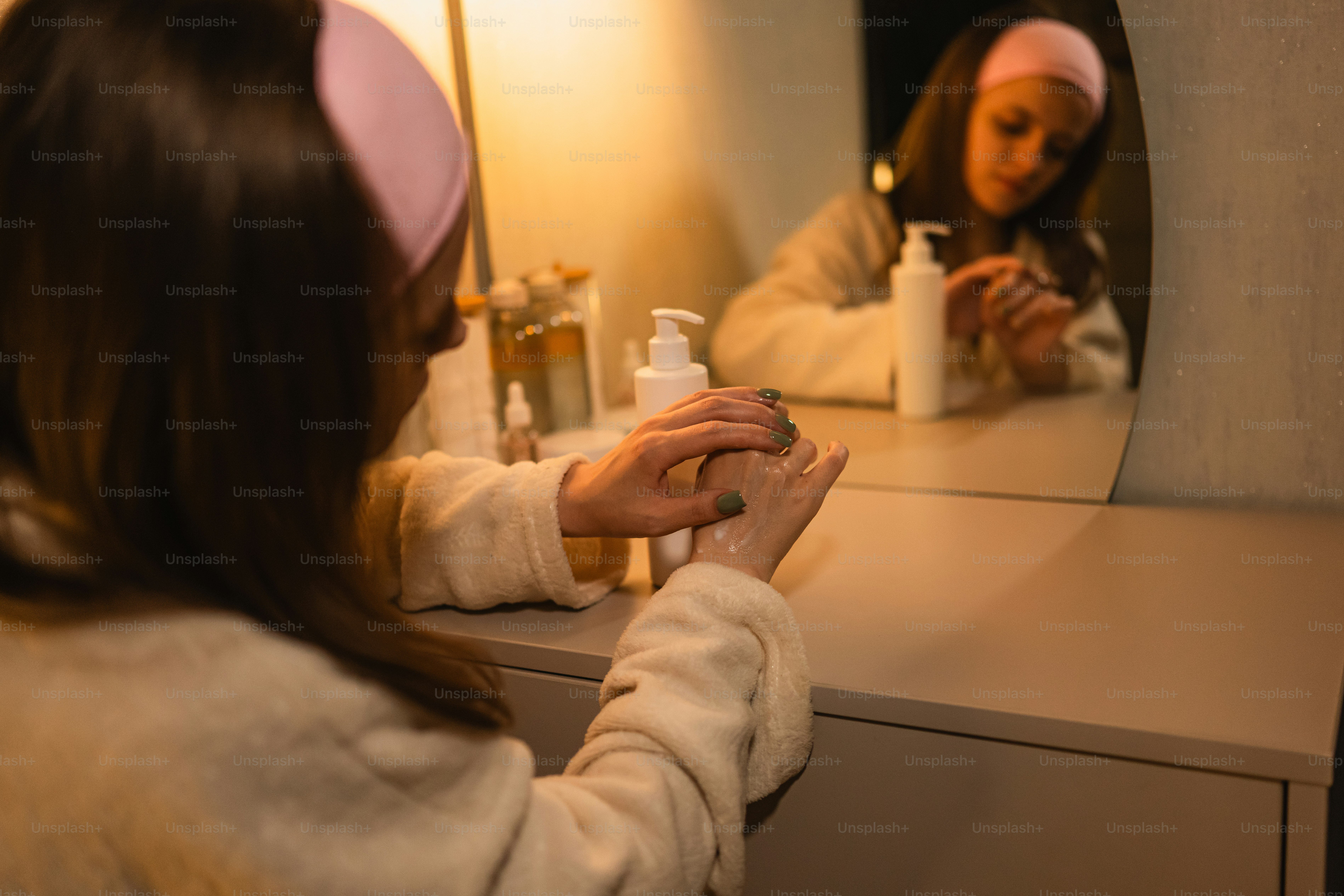 Young woman applying lotion to her hands at vanity