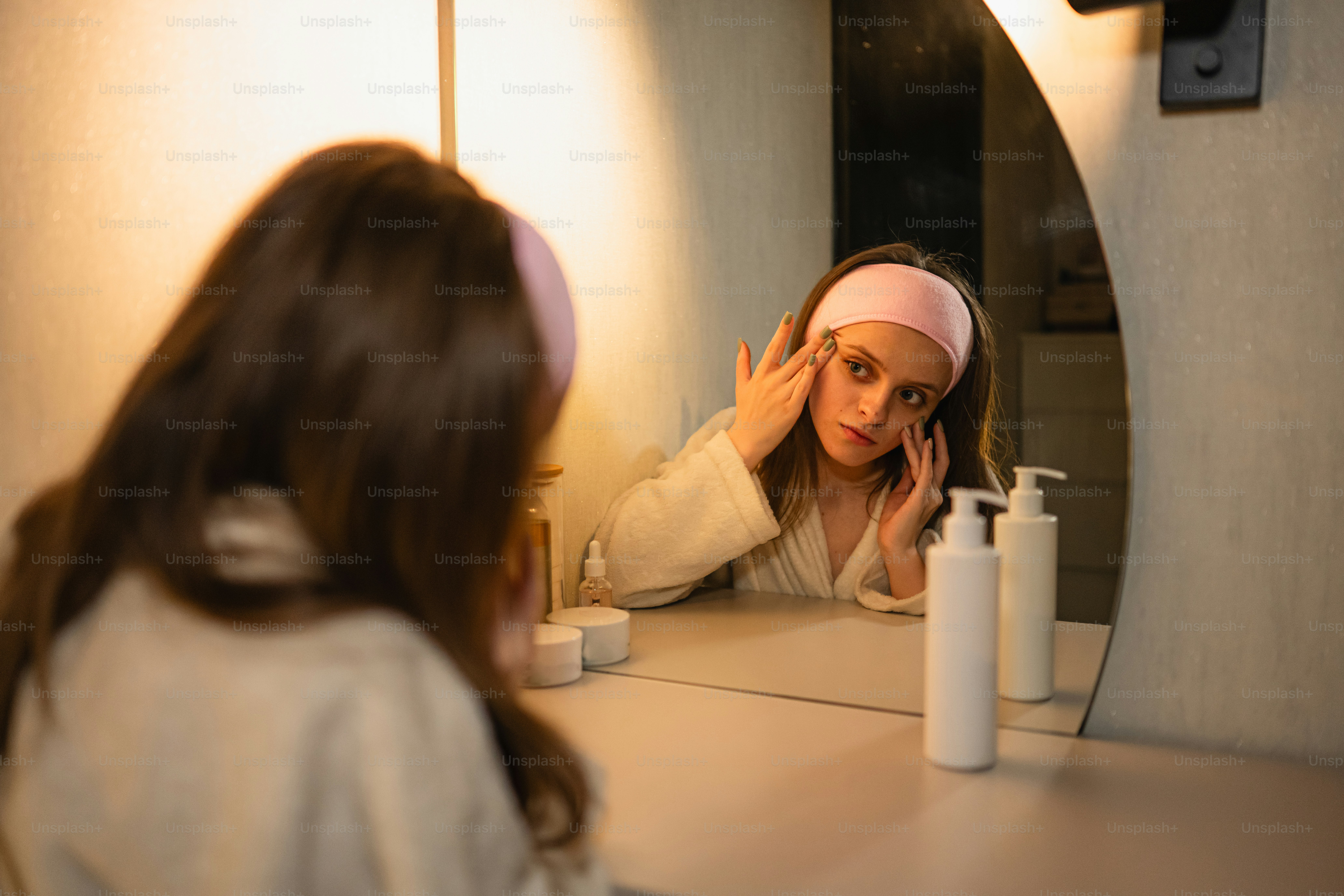 Young woman applying skincare in front of mirror