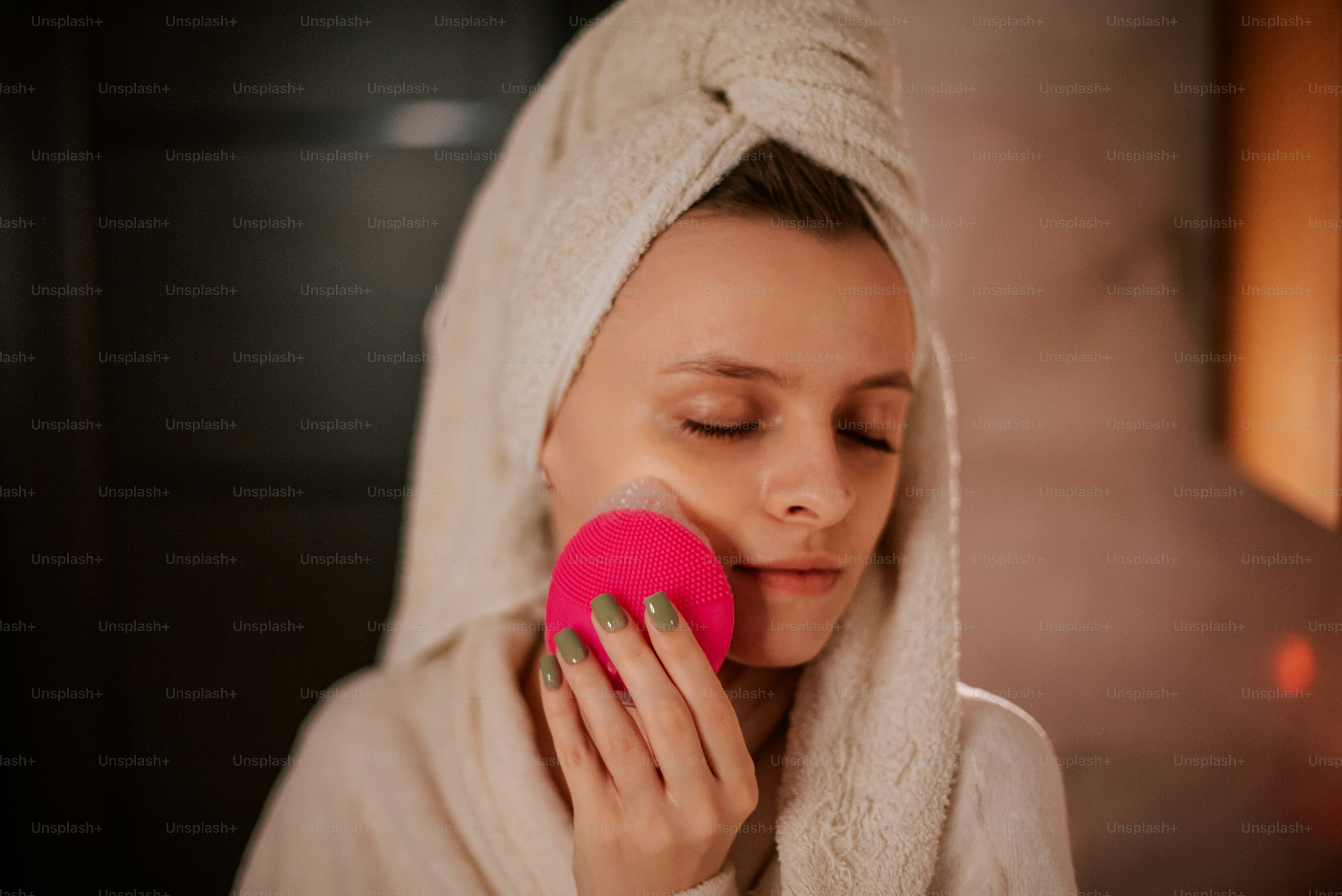 Woman cleansing face with pink facial brush.