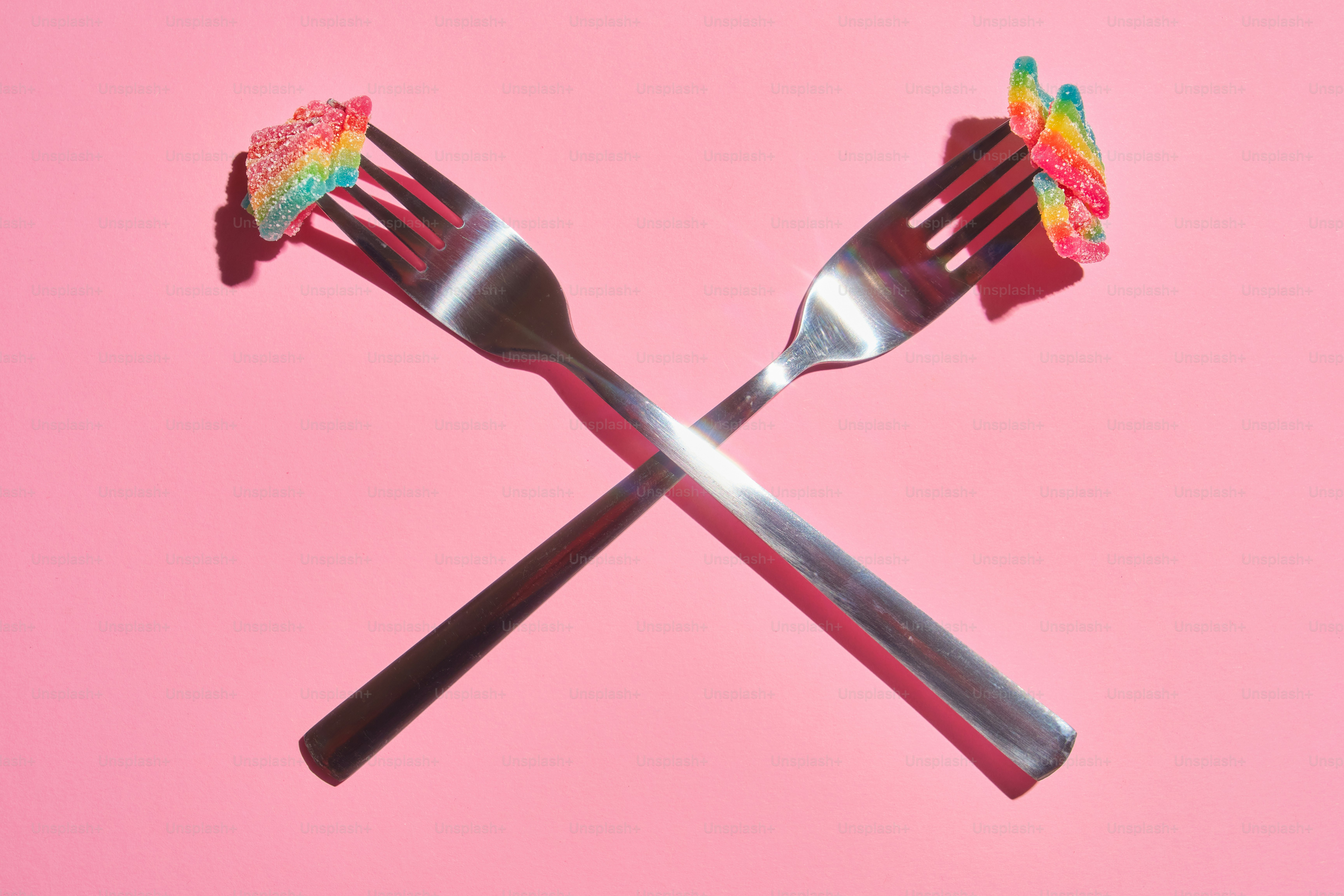 Two forks with rainbow candies on pink background
