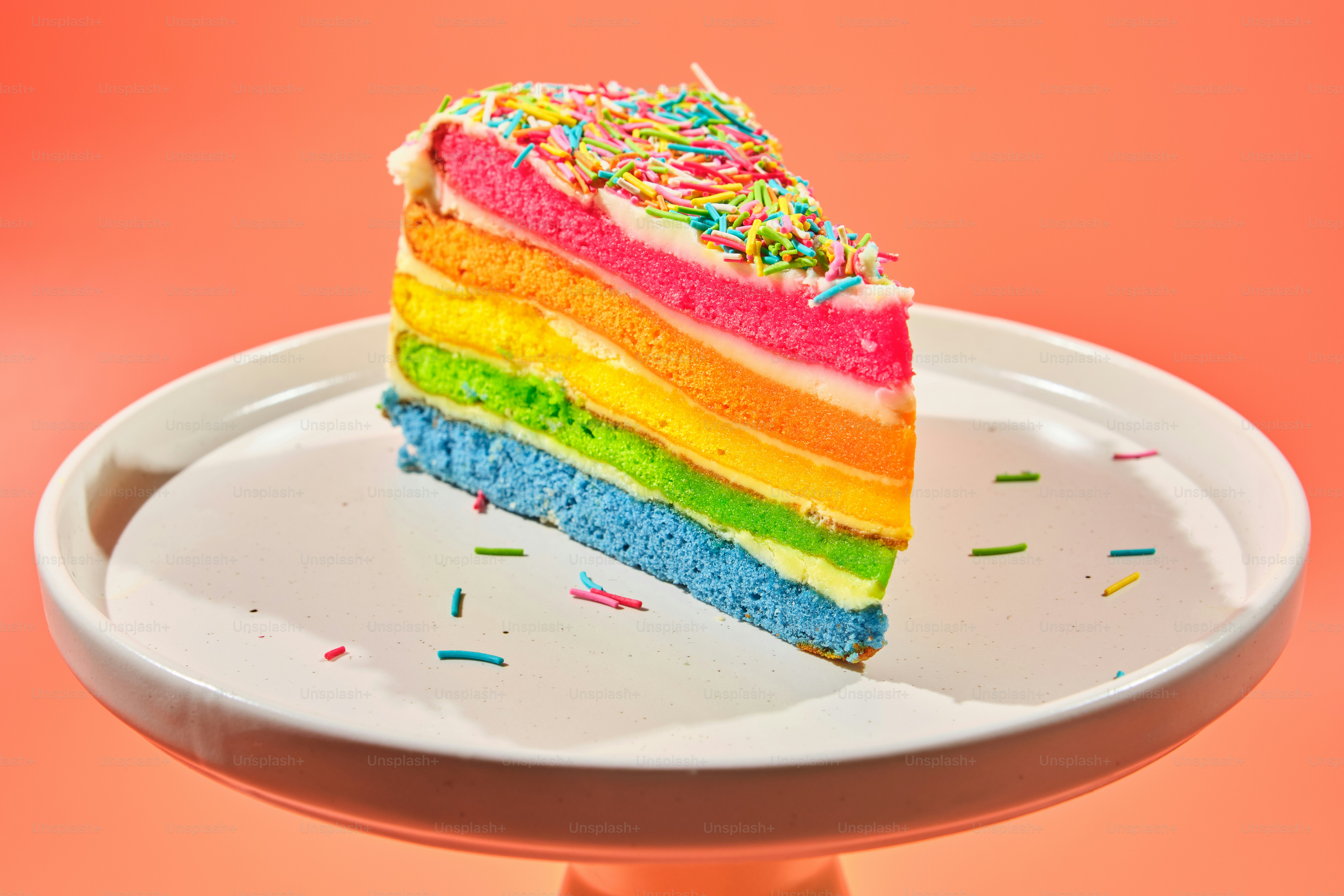 A slice of rainbow cake with sprinkles on a stand