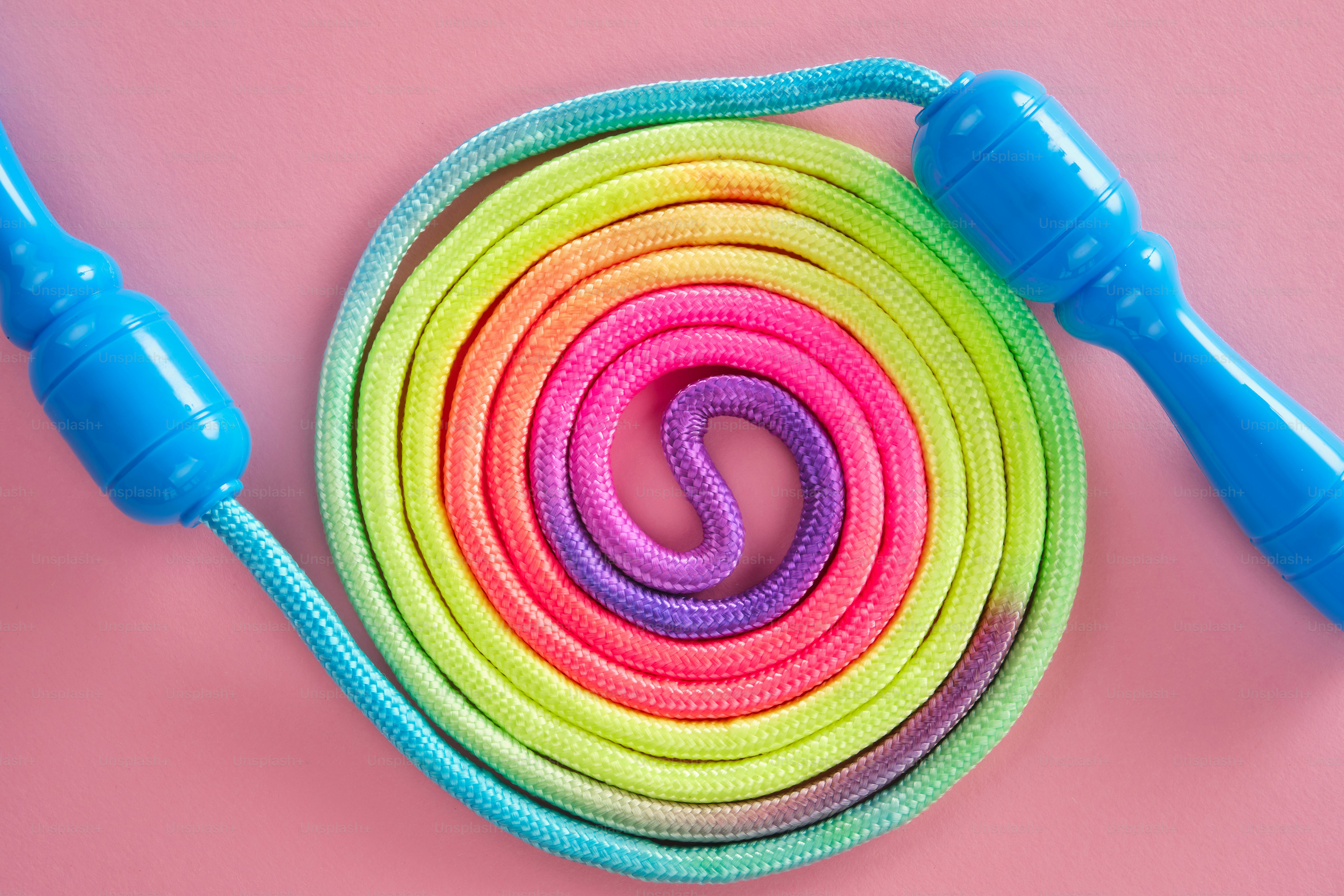 A colorful jump rope coiled on a pink background