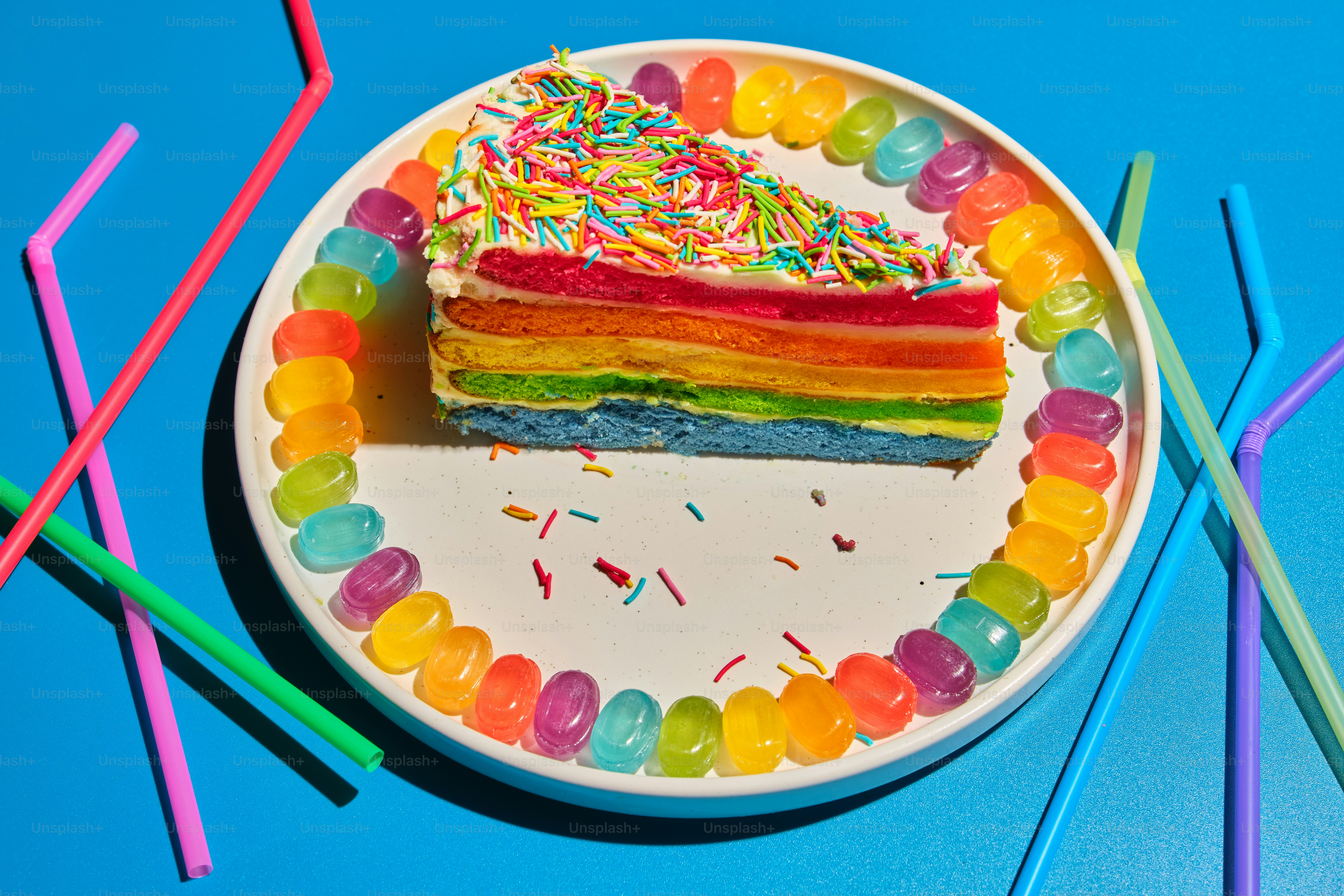 Slice of rainbow cake with colorful candy and straws