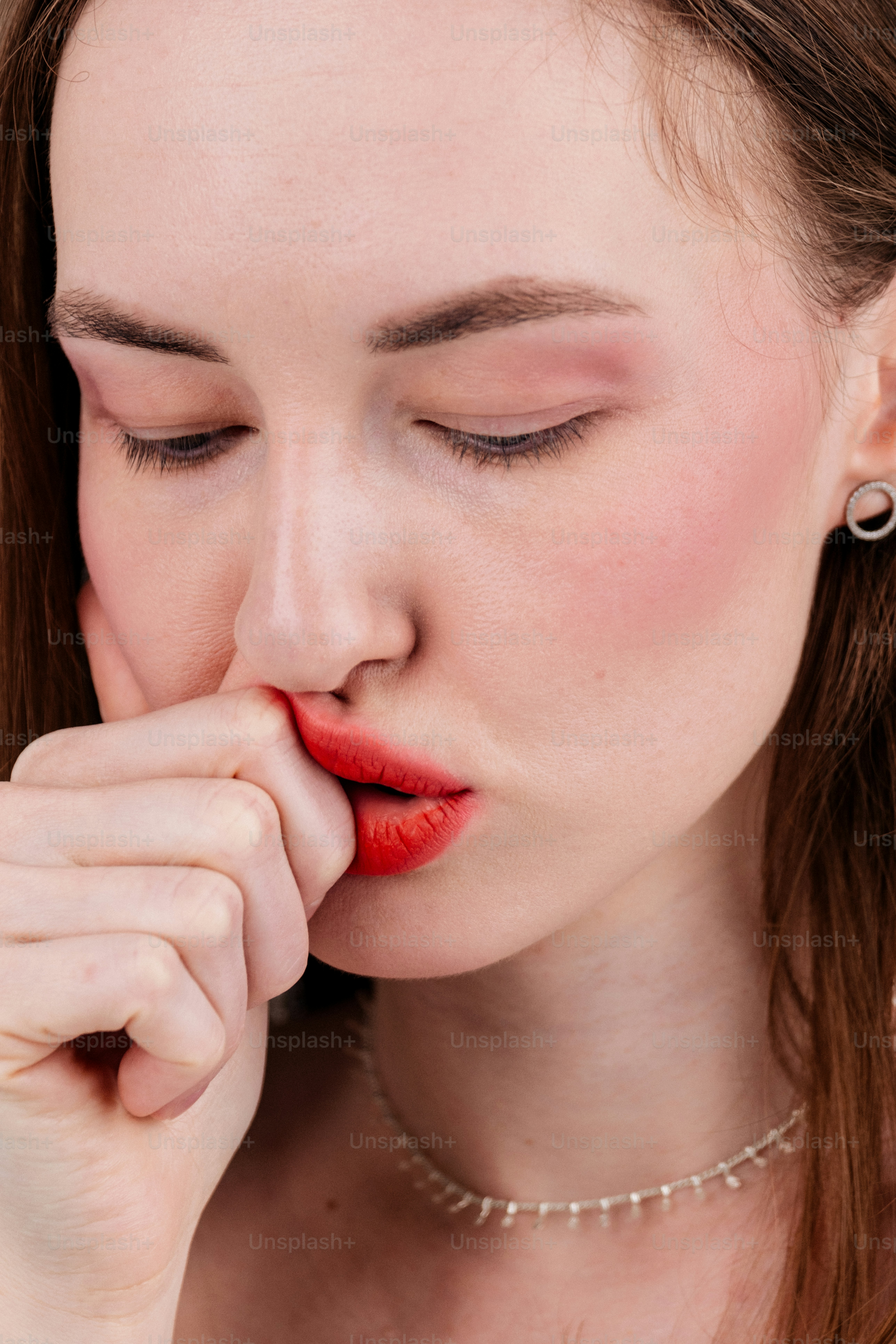 Mujer con pintalabios rojo mordiéndose el dedo.