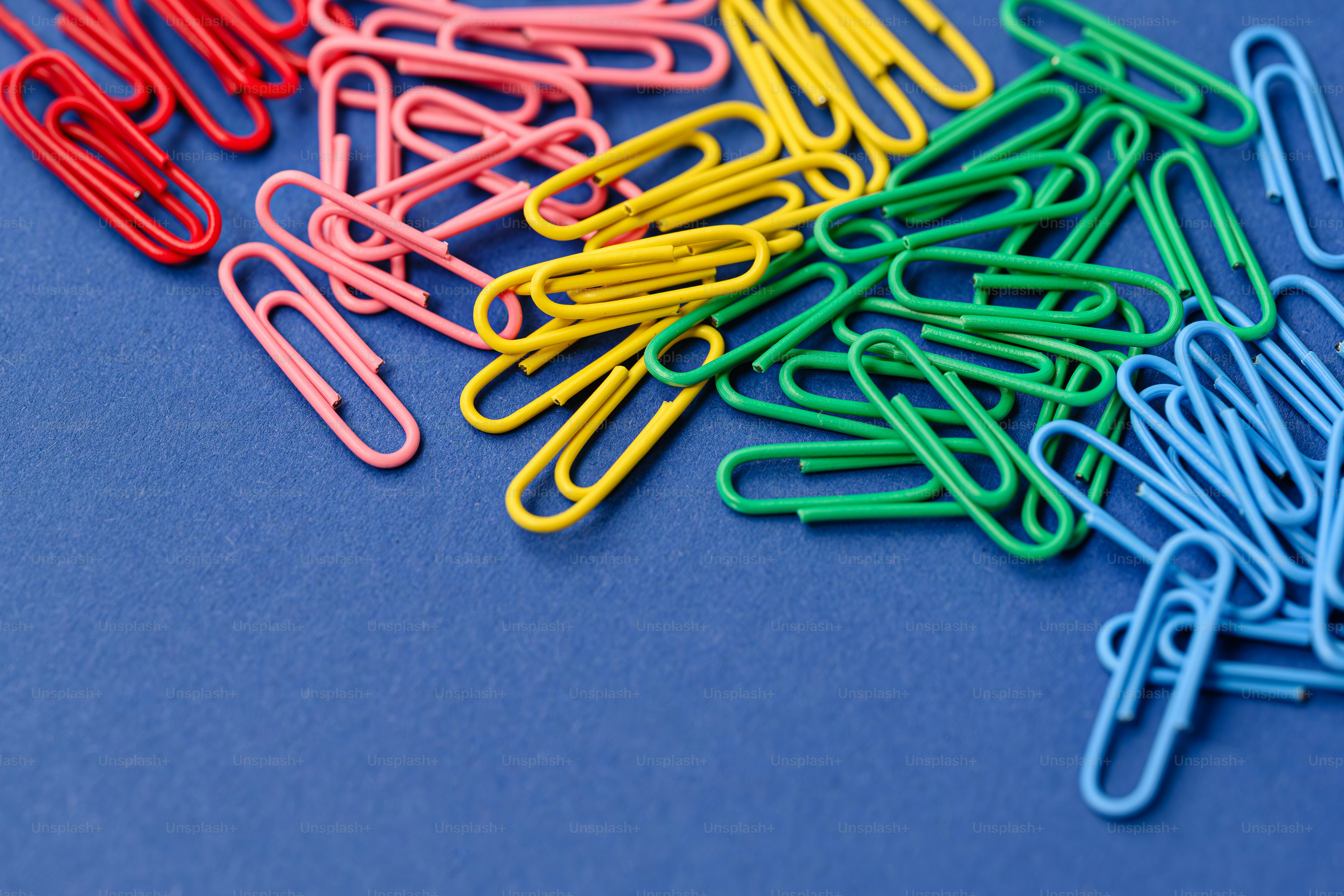 Bunte Büroklammern auf einer blauen Oberfläche verstreut.