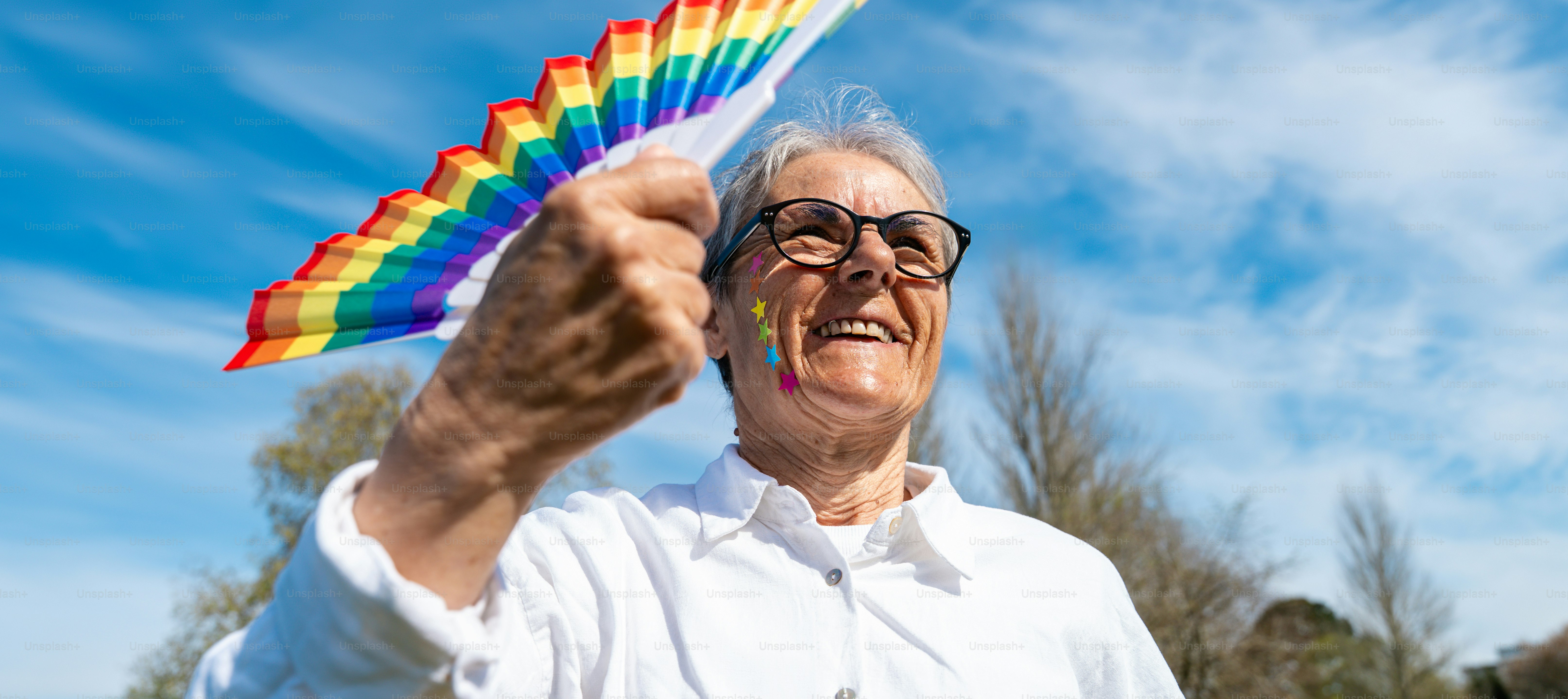 Personne âgée tenant un drapeau arc-en-ciel contre un ciel bleu