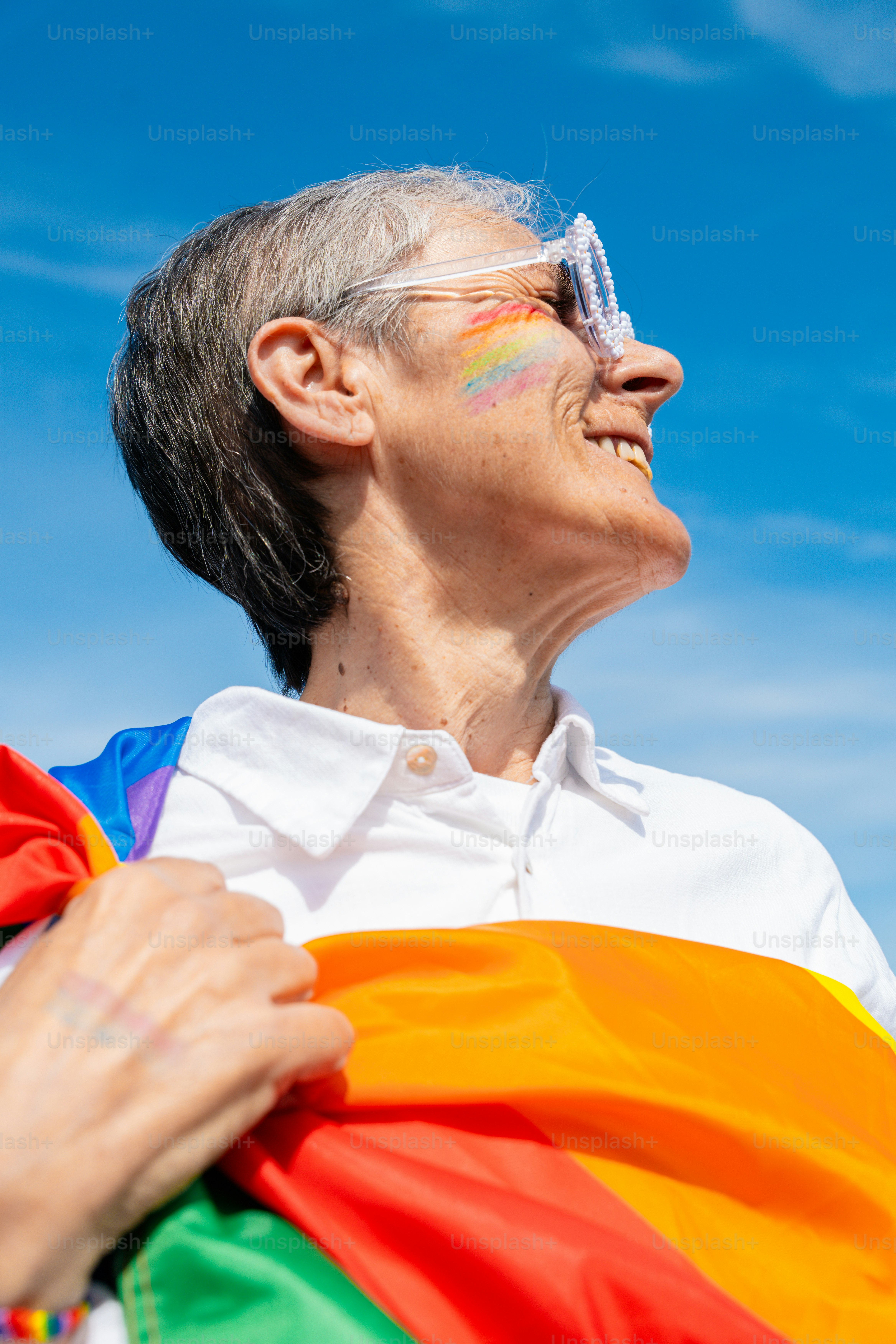 Personne avec un drapeau arc-en-ciel et un maquillage facial sourit joyeusement peinte