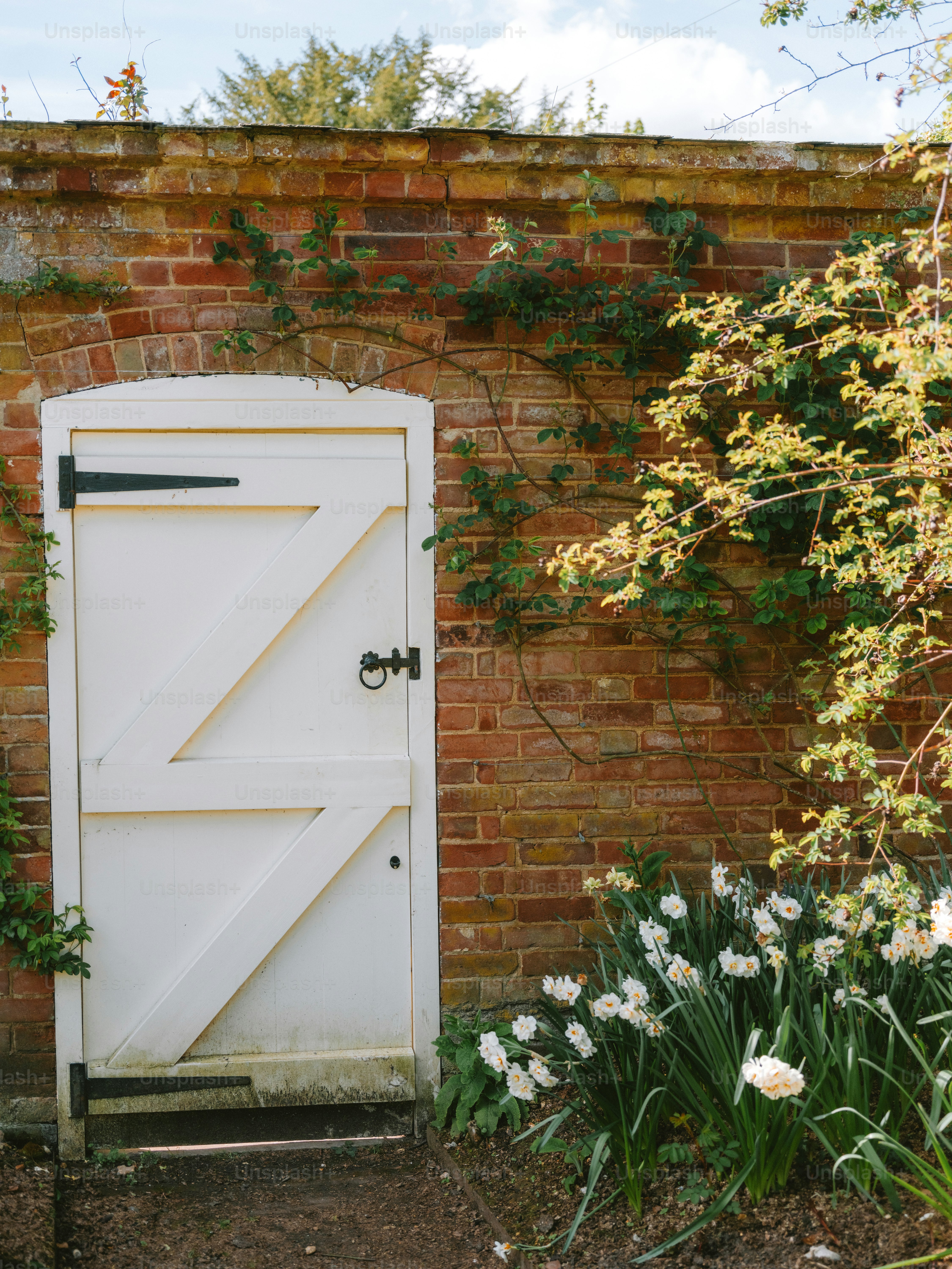 White door set in a brick wall with flowers.