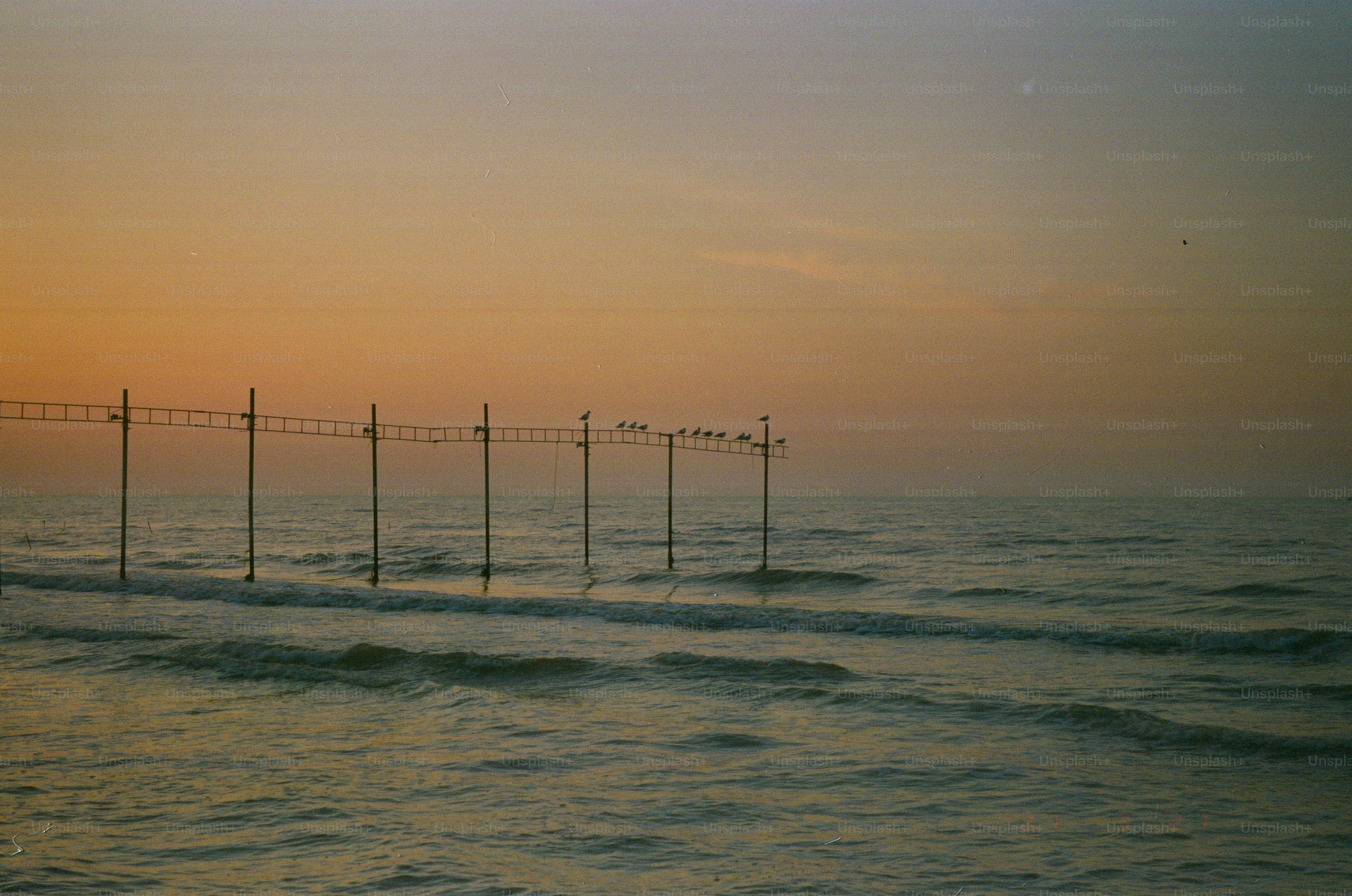 Ocean waves under a hazy sunset sky with poles