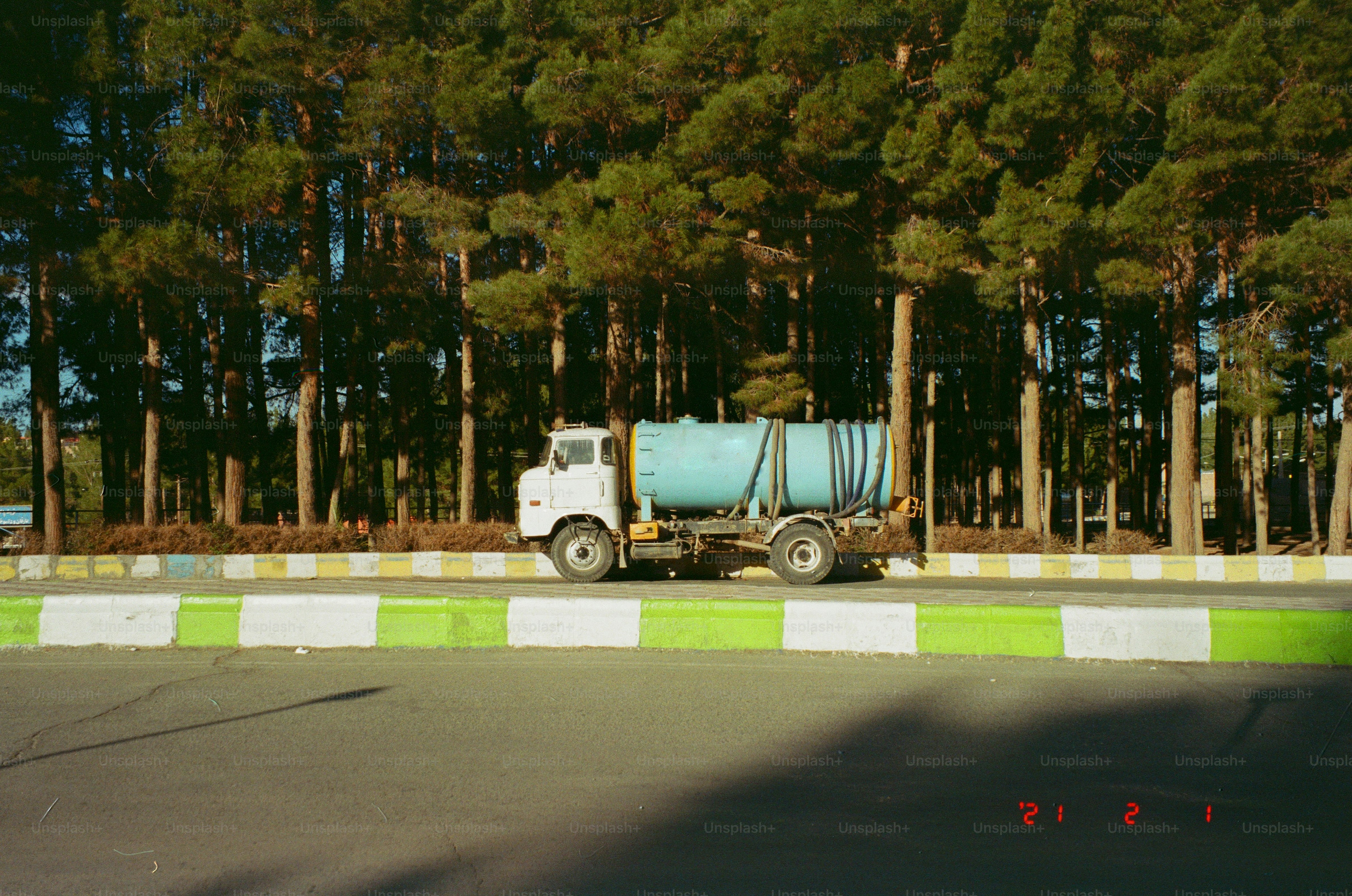 A water truck drives past a line of tall trees