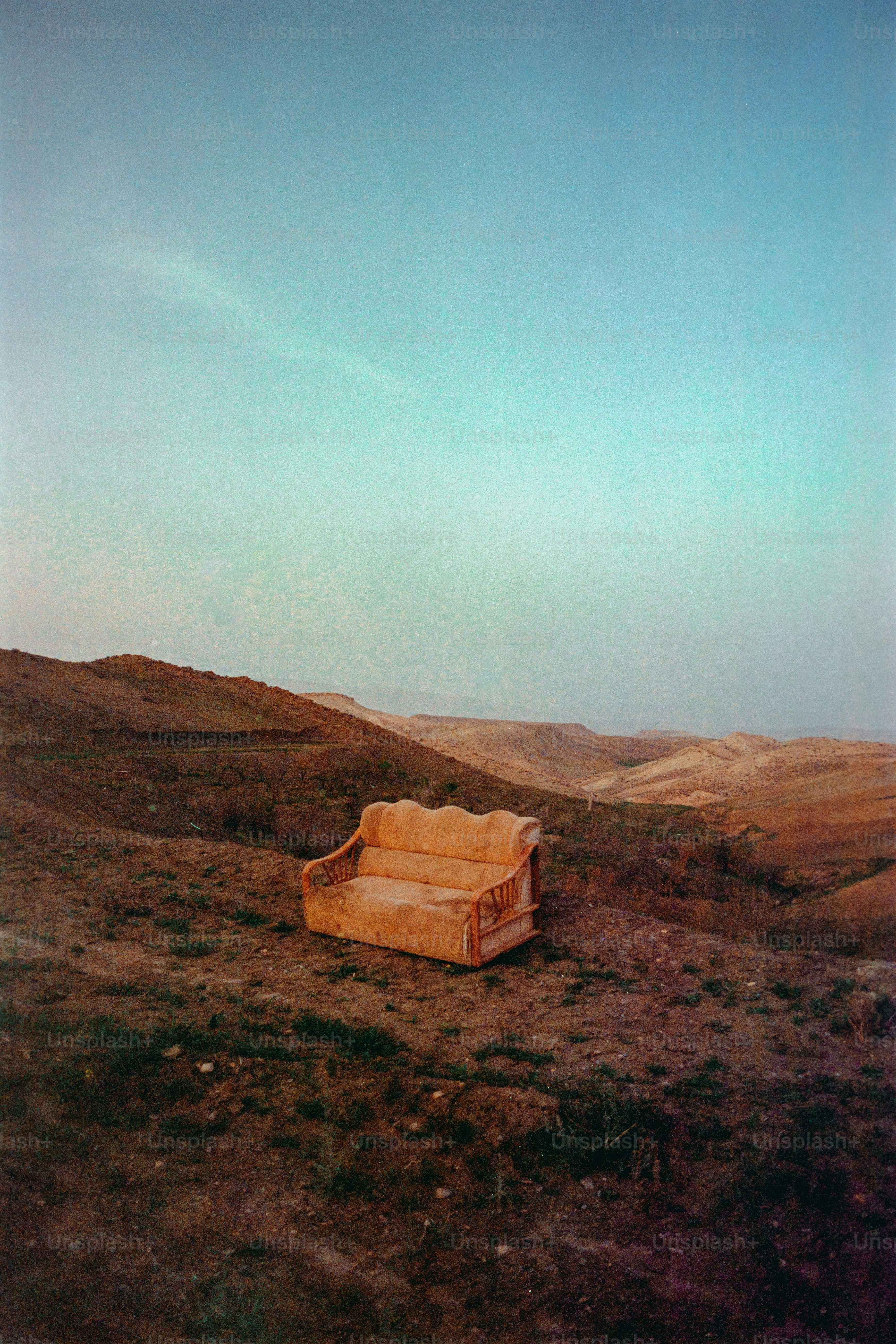 An orange couch sits alone on a barren hillside