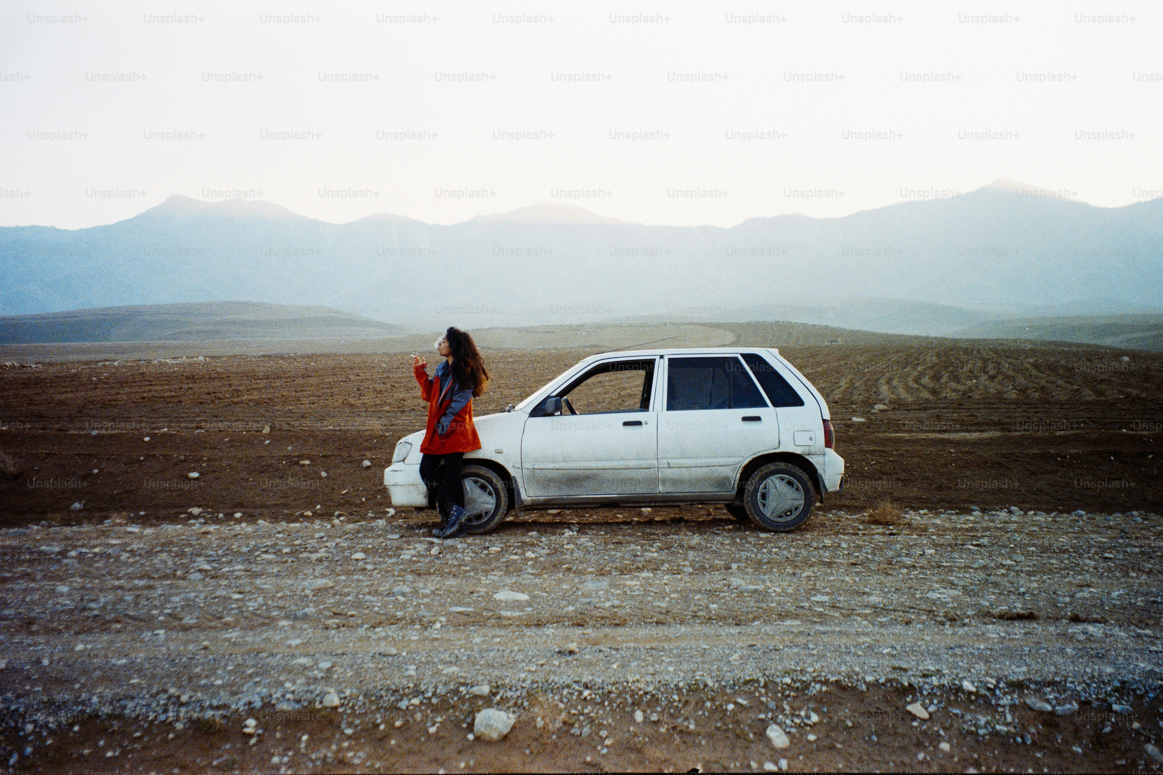 Femme en veste rouge appuyée sur une voiture dans un paysage désolé