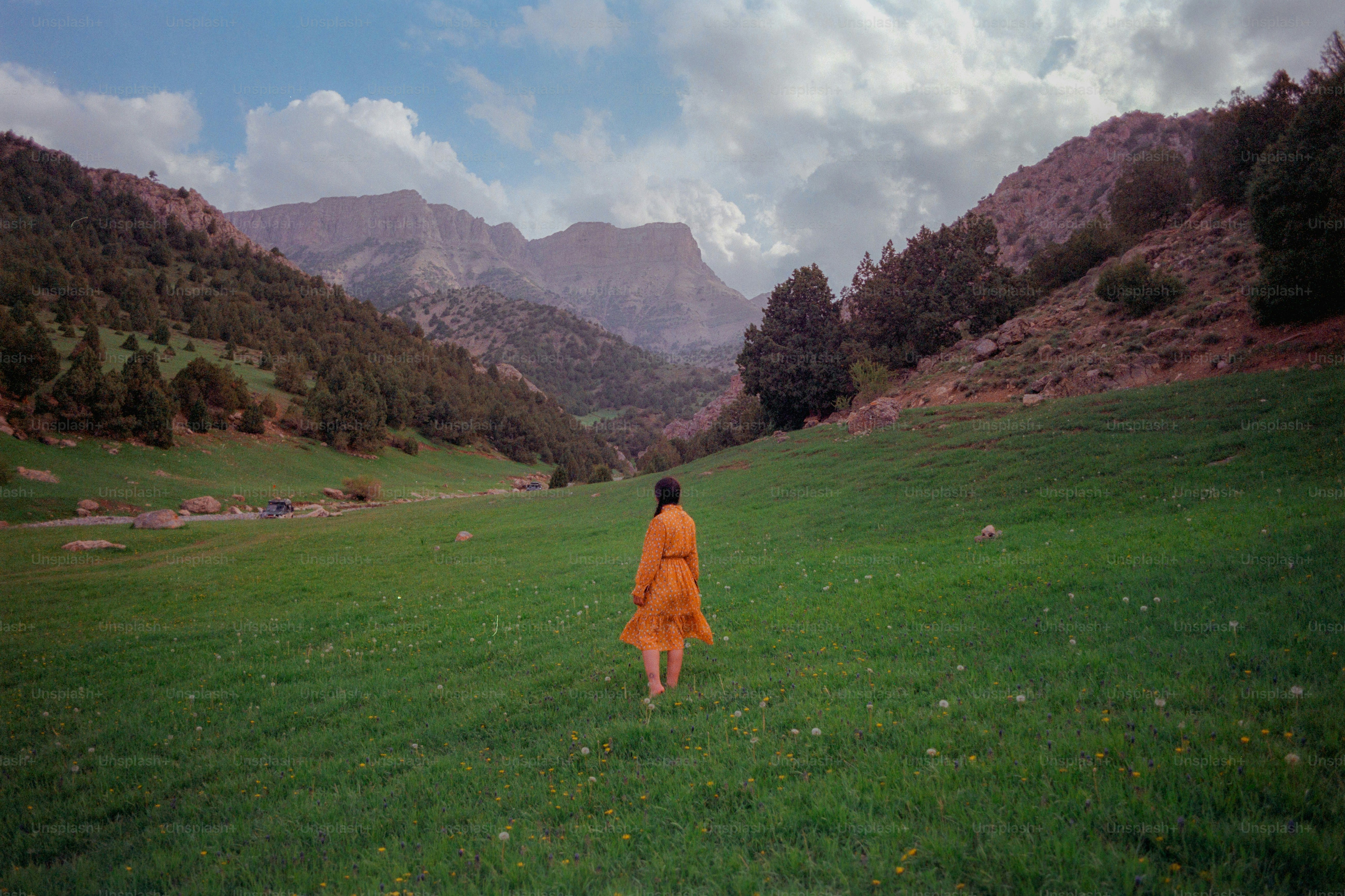 Woman in orange dress walks through green mountain valley