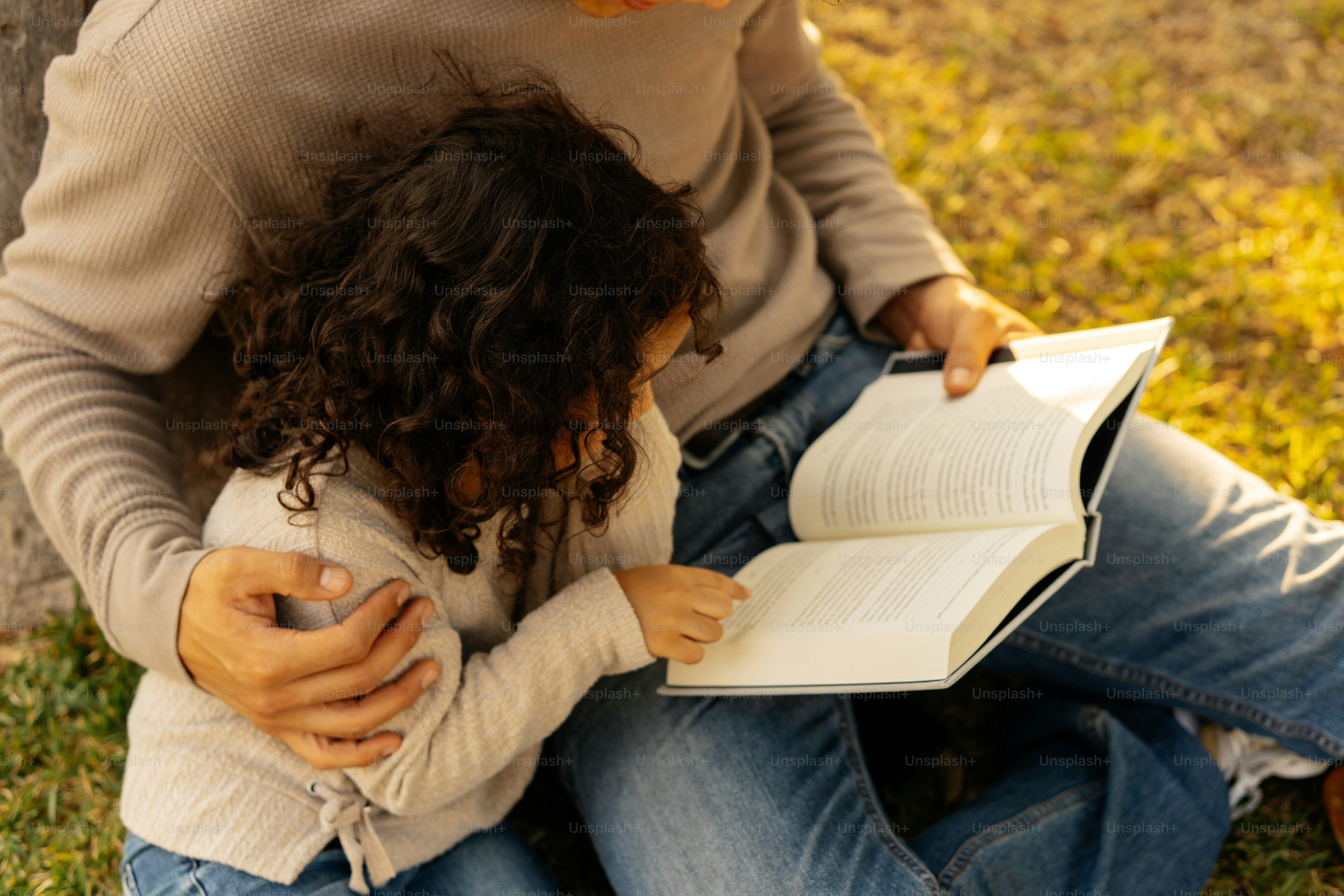 Père et fille lisant un livre ensemble en plein air.