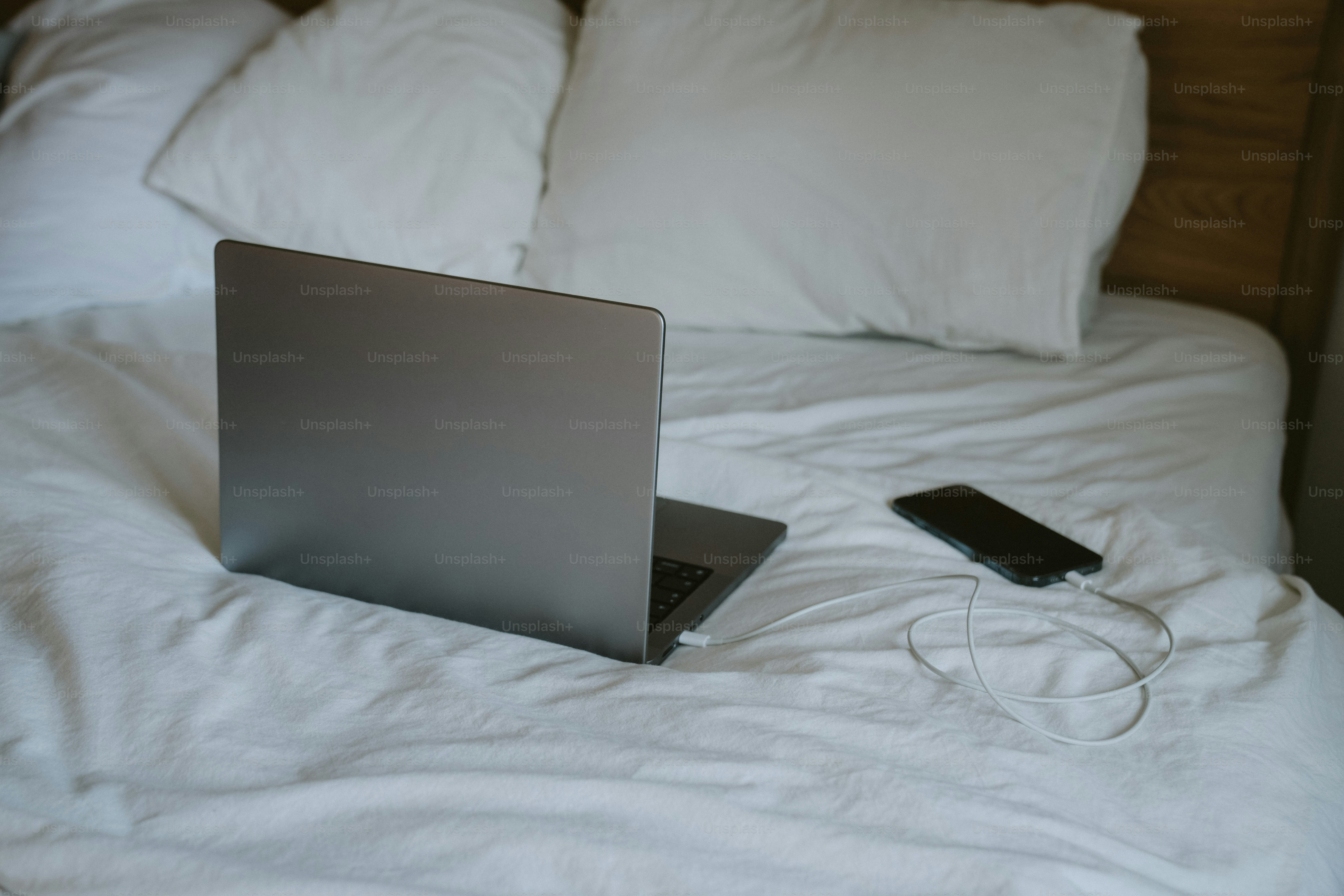 Laptop e telefono su un letto bianco accartocciato.