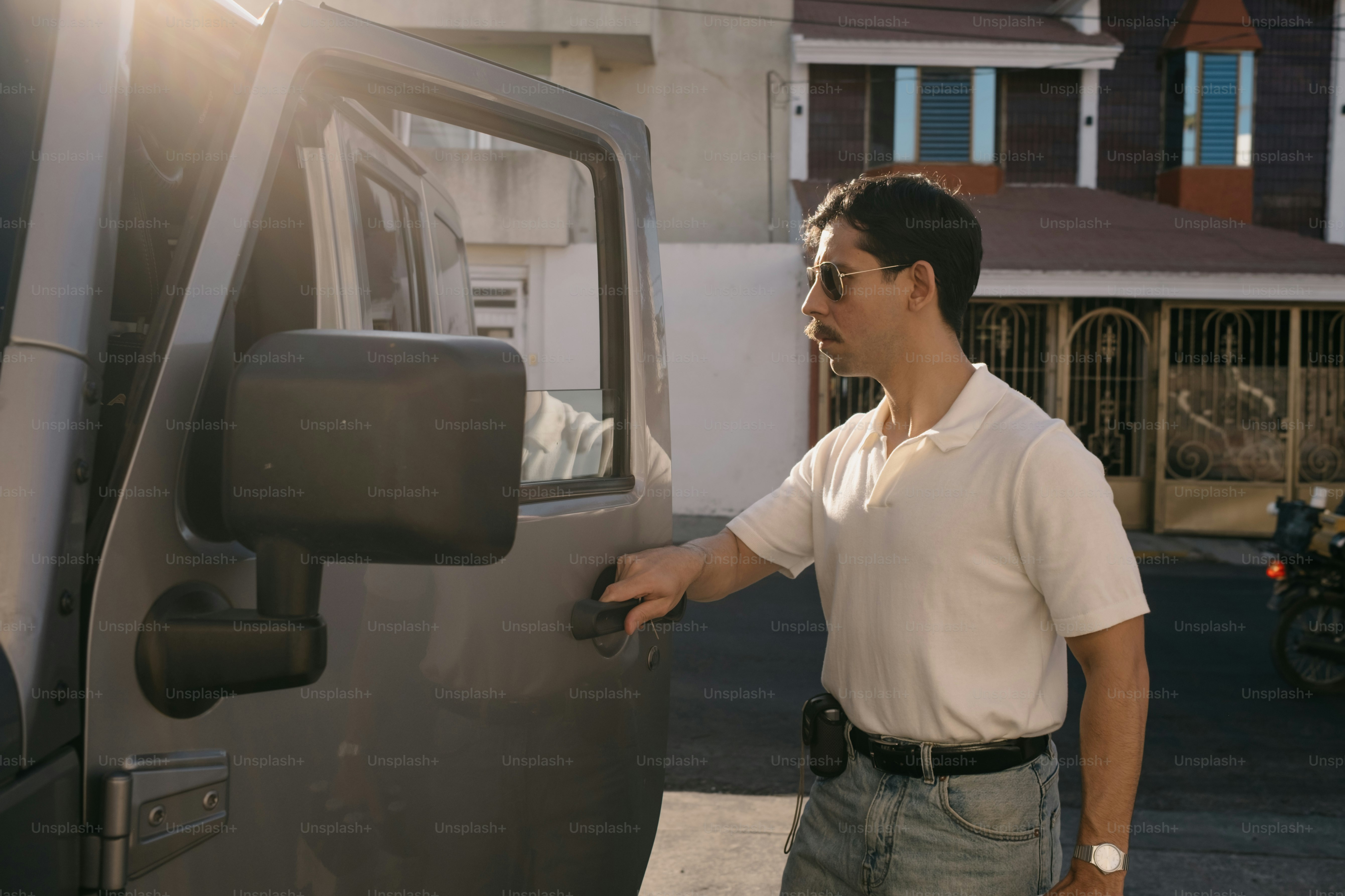 Man in white shirt opens car door in sunlight