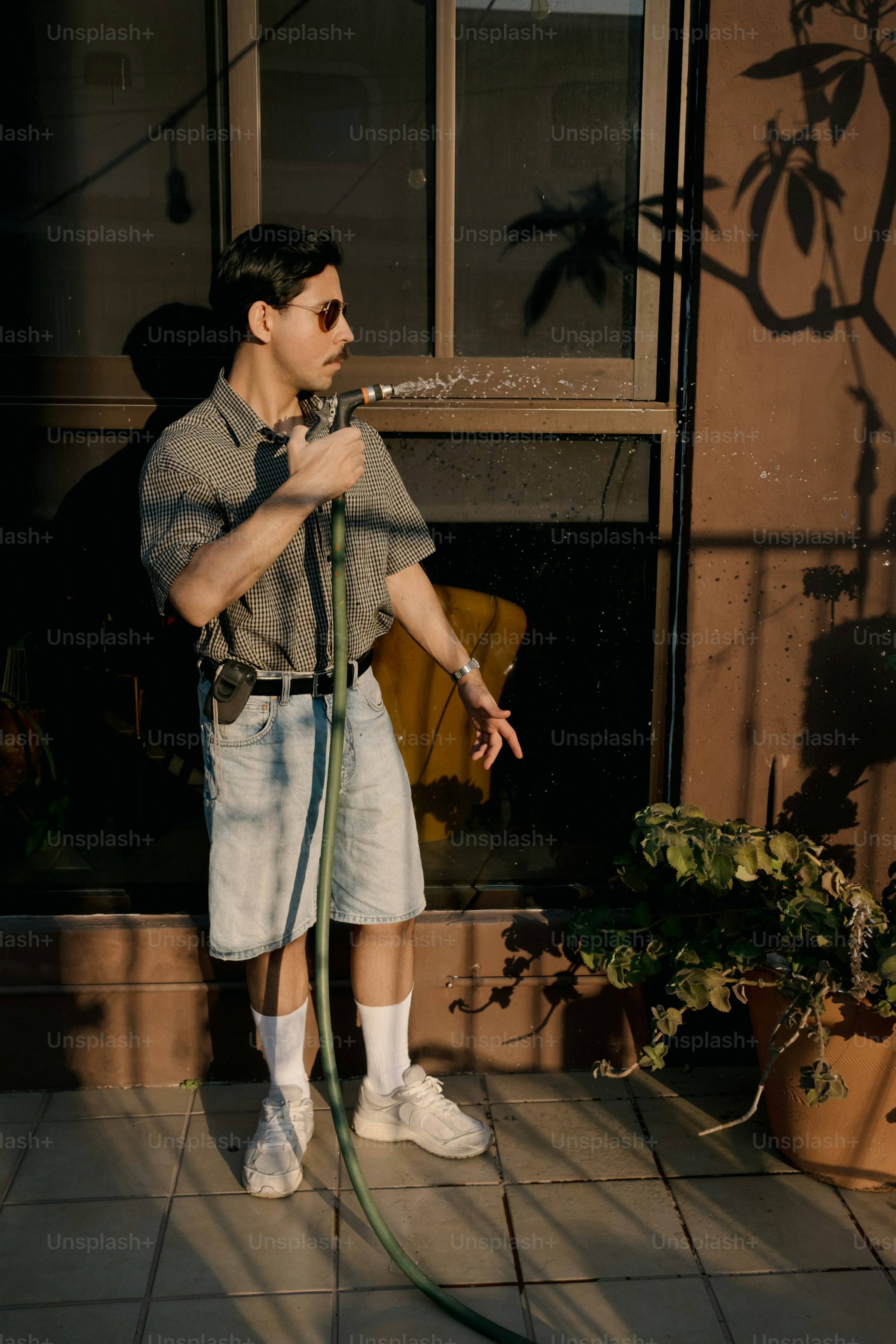Man in shorts watering plants with a hose