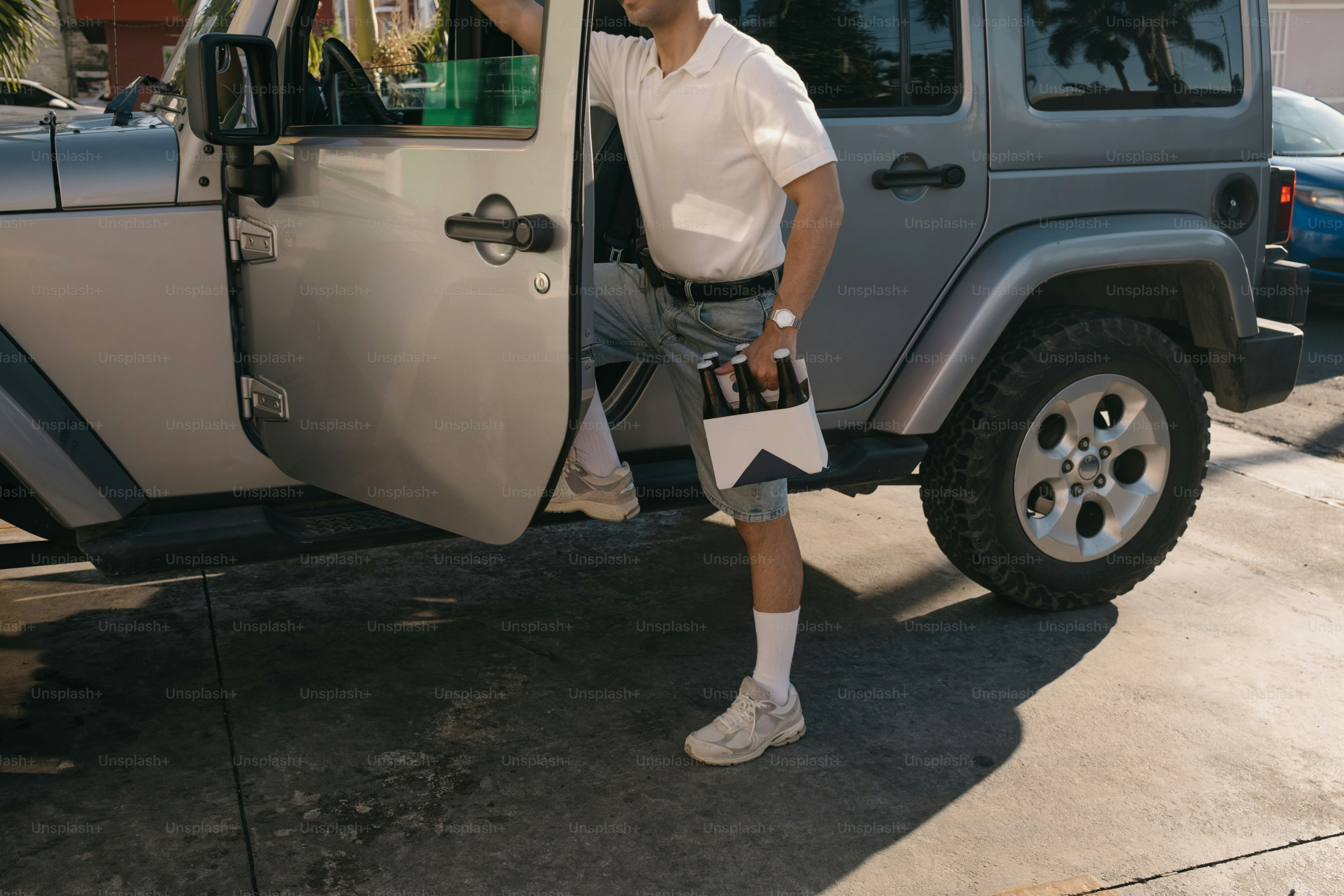 Hombre que lleva cerveza saliendo de un jeep plateado