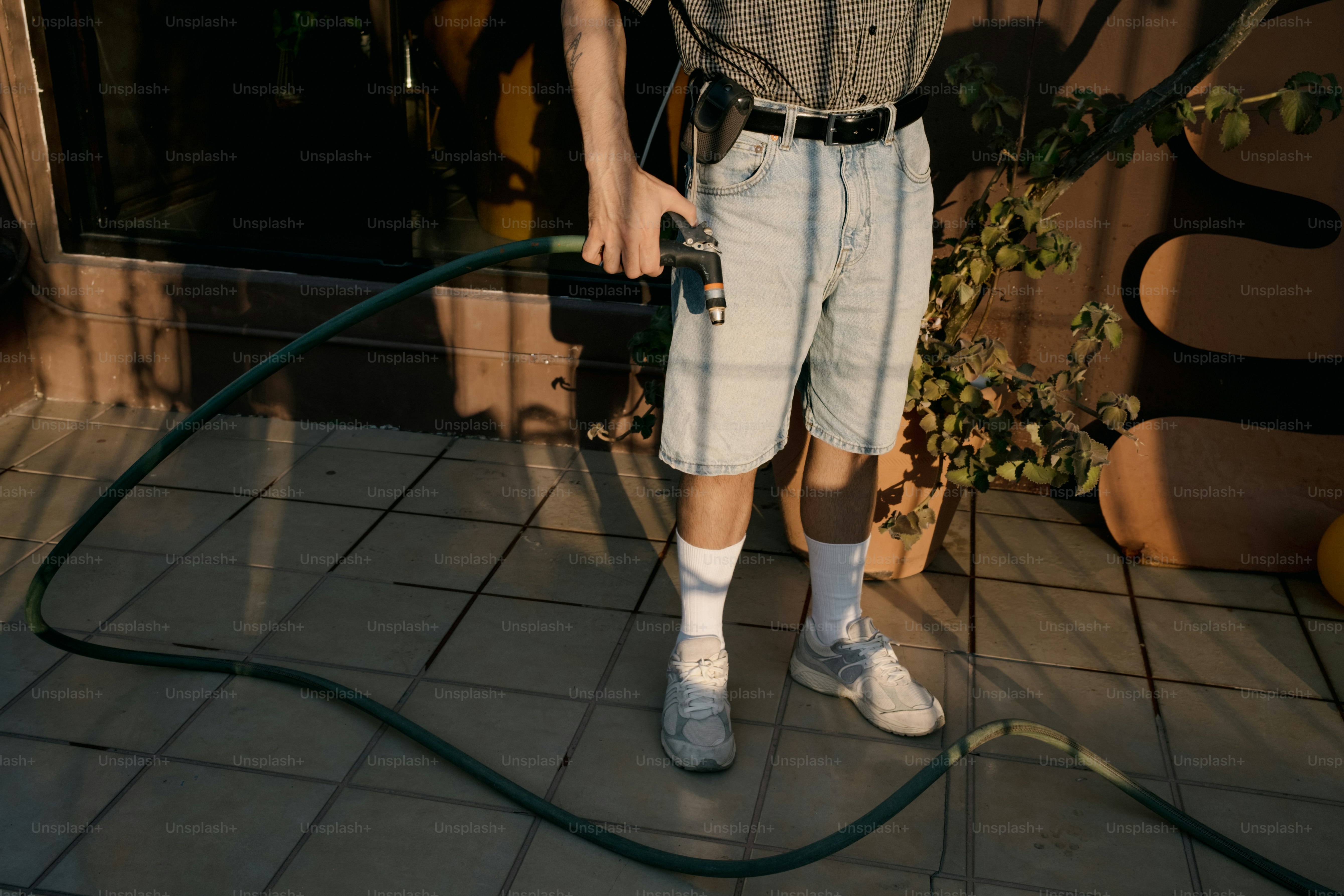 Homme tenant un tuyau d’arrosage sur une terrasse carrelée