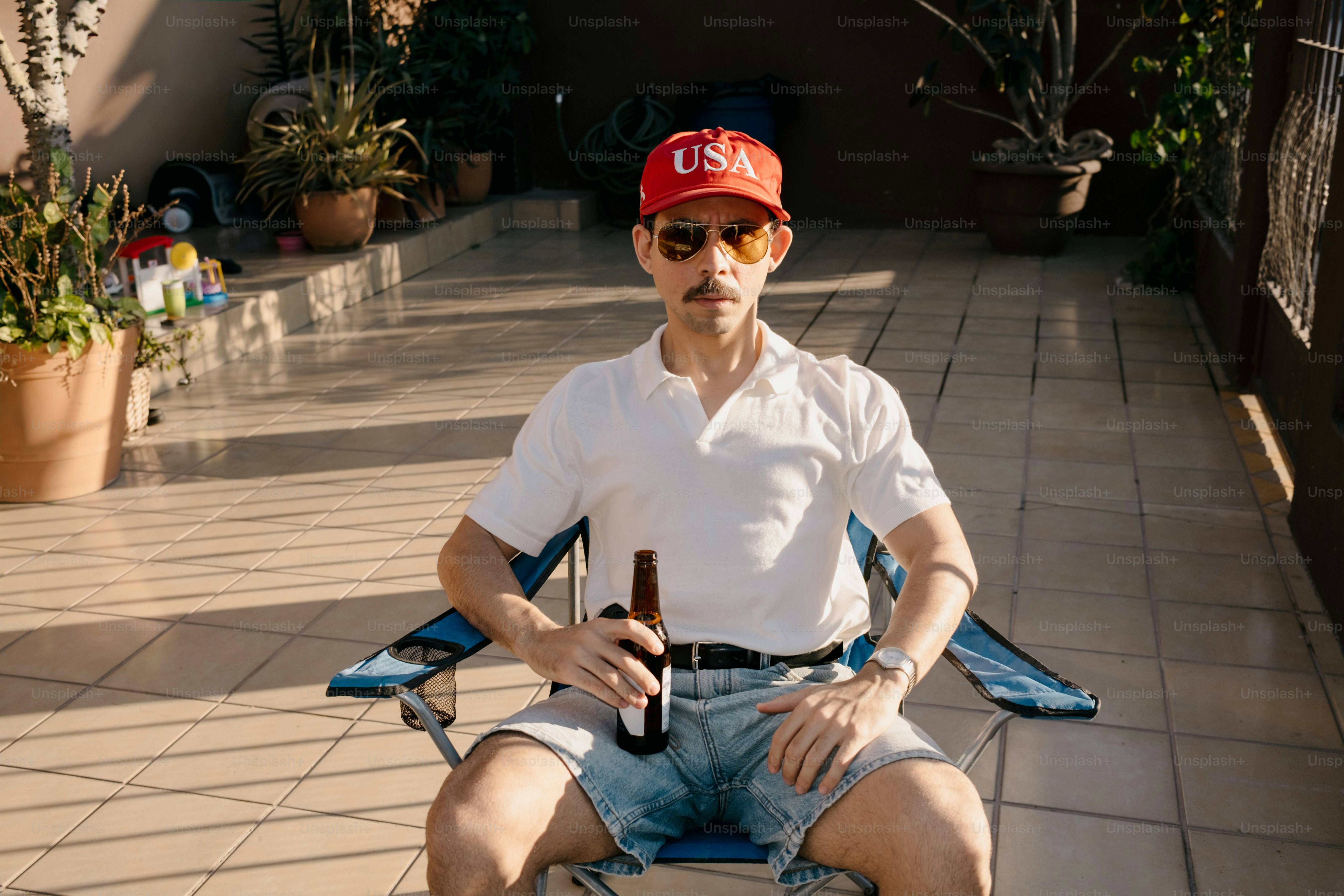 Man in usa hat and sunglasses holds beer on patio