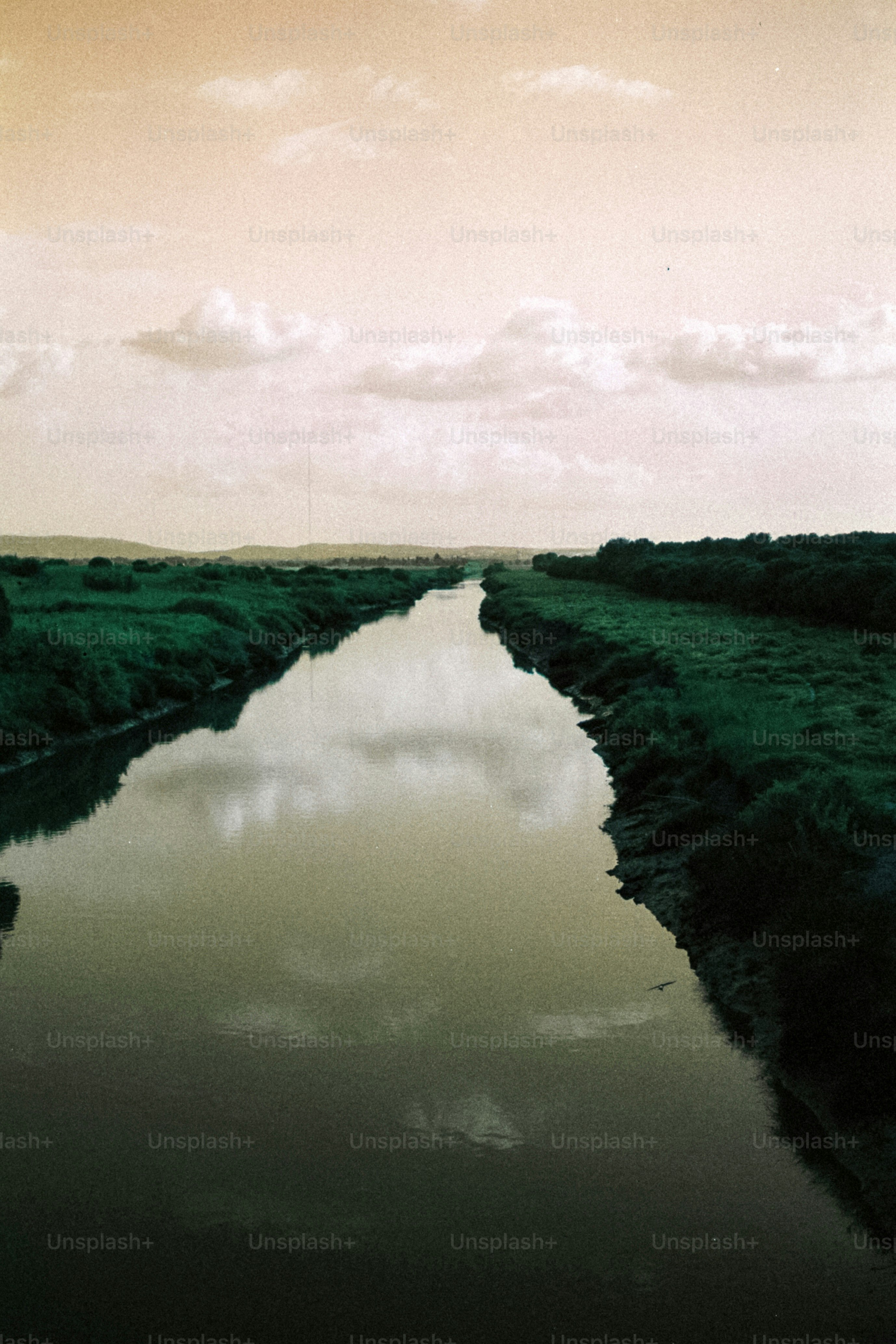 A calm river reflects the cloudy sky and green banks.