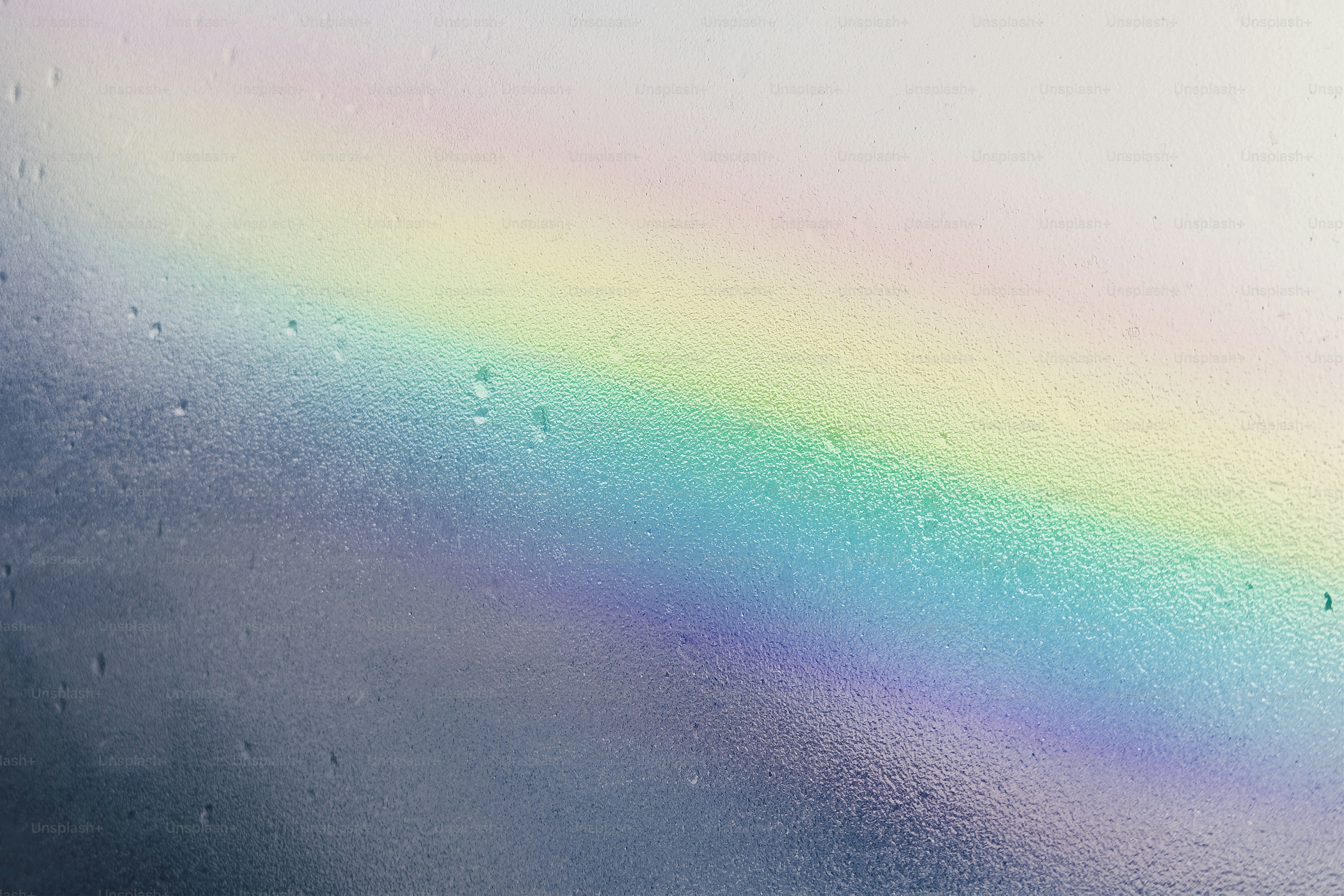 A faint rainbow appears through water droplets on glass.