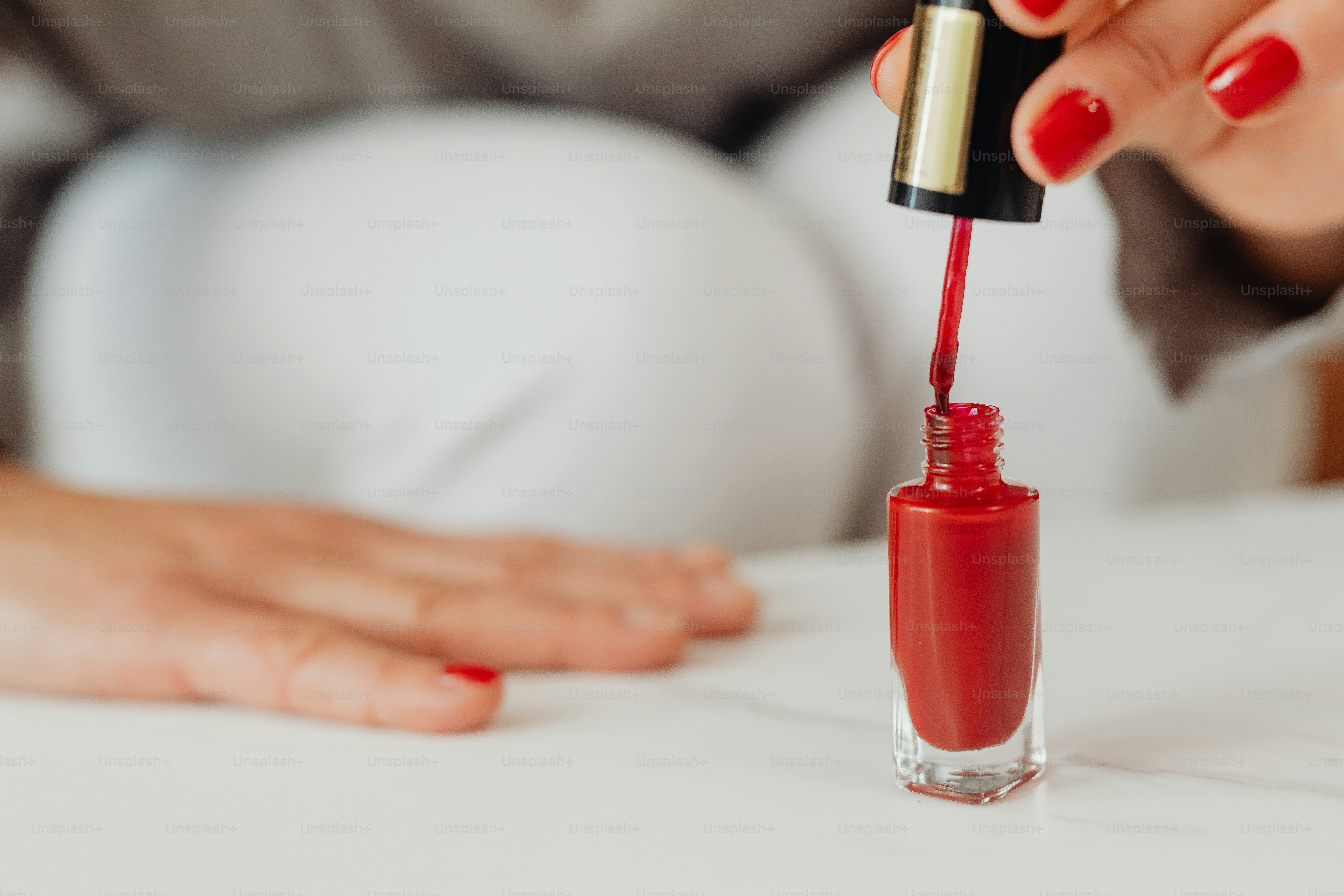 Femme qui applique du vernis à ongles rouge sur son ongle.
