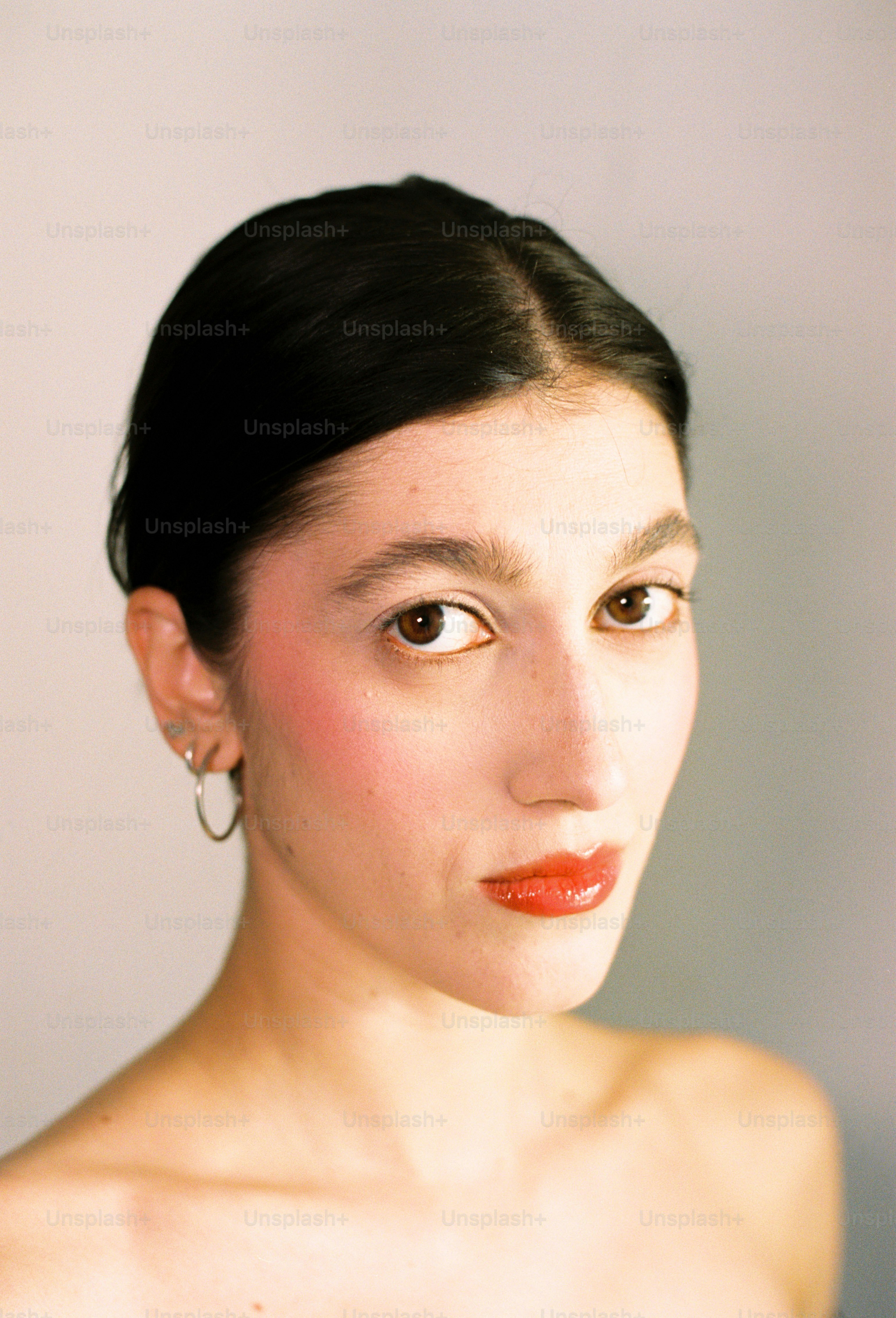 A woman with dark hair and red lipstick looks forward.