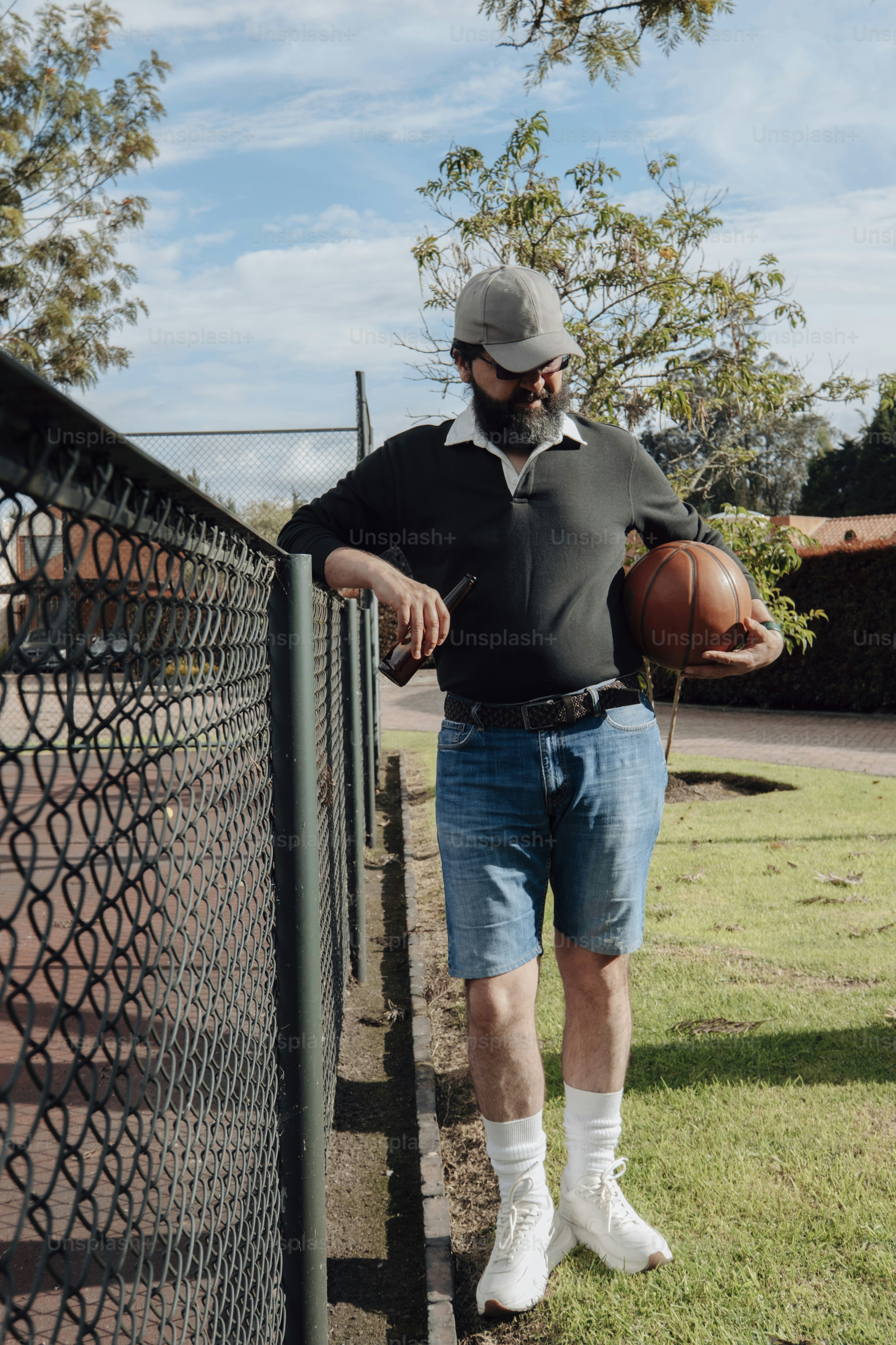Homme en short tenant un ballon de basket près d’une clôture