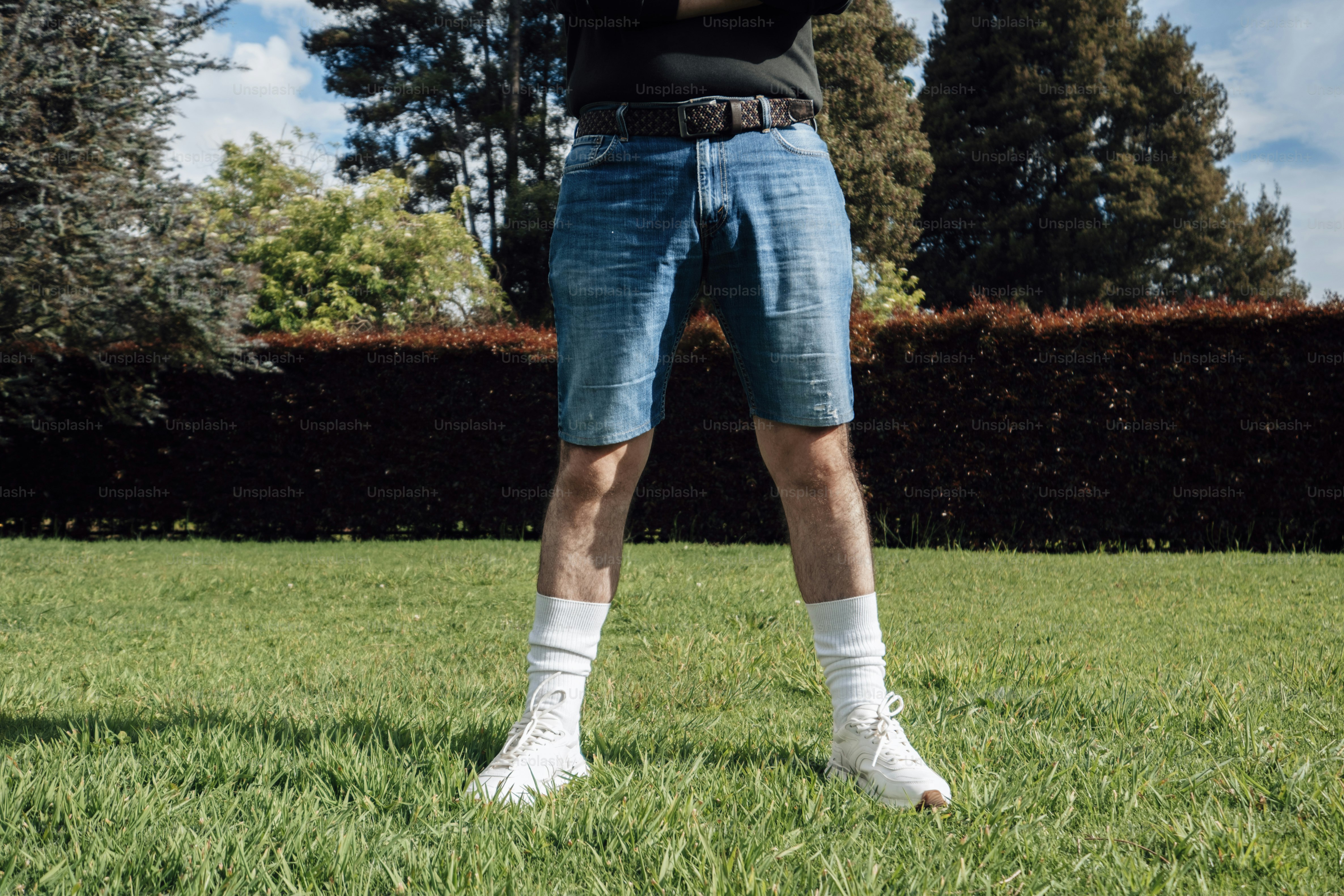 Homme en short en jean et chaussettes blanches, debout sur l’herbe