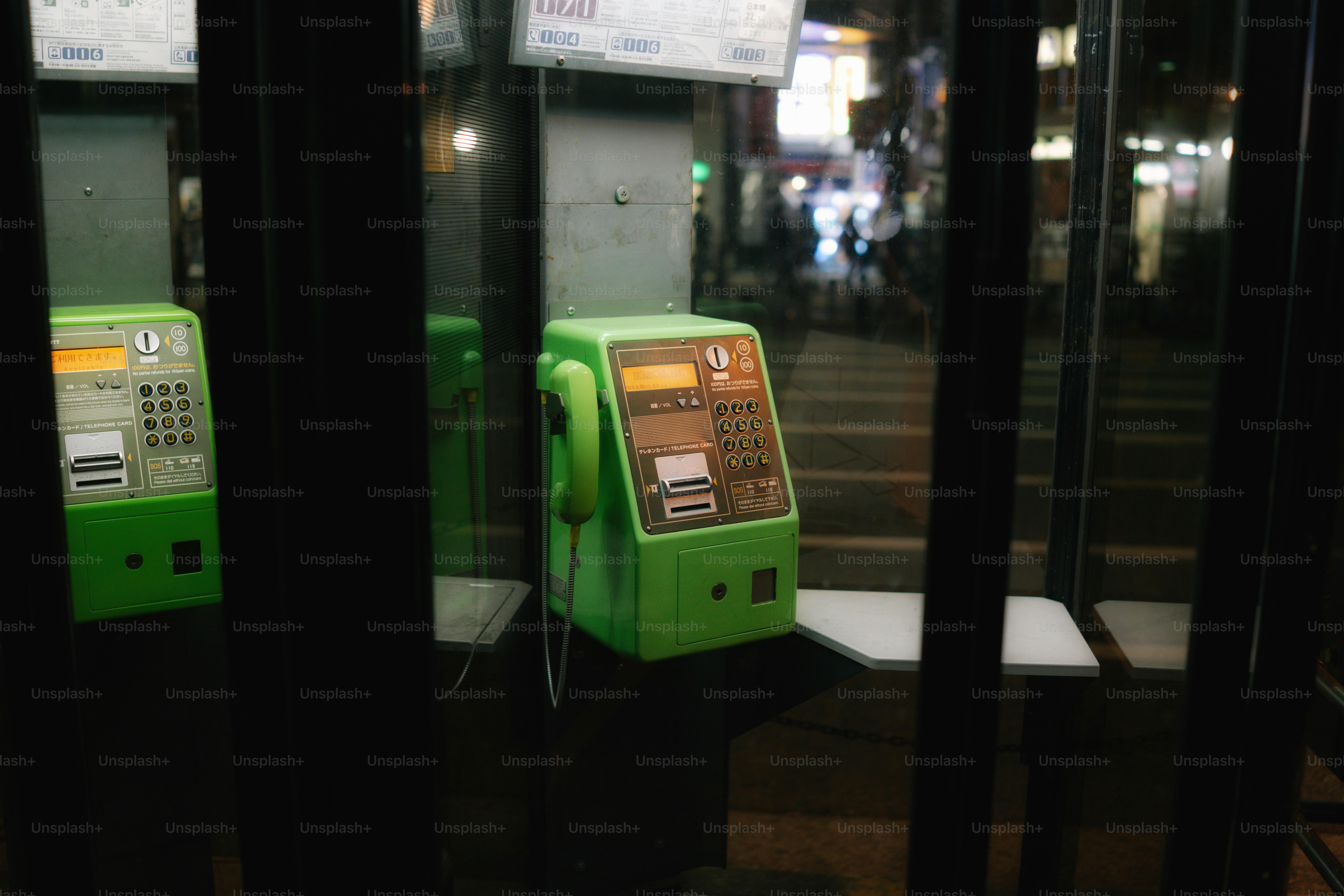 Zwei grüne Telefonzellen auf einer Stadtstraße bei Nacht.