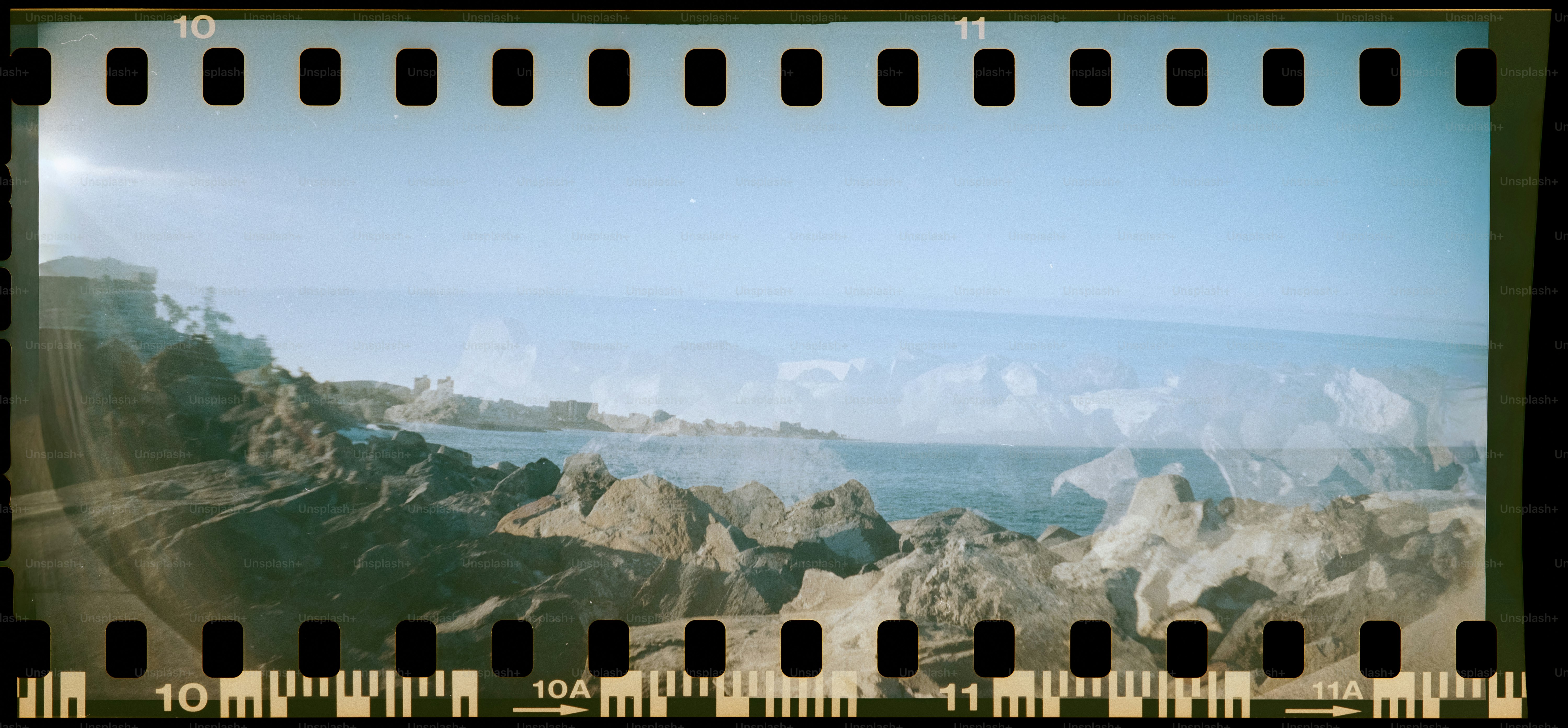 Rocky coastline with mountains in background under a clear sky.