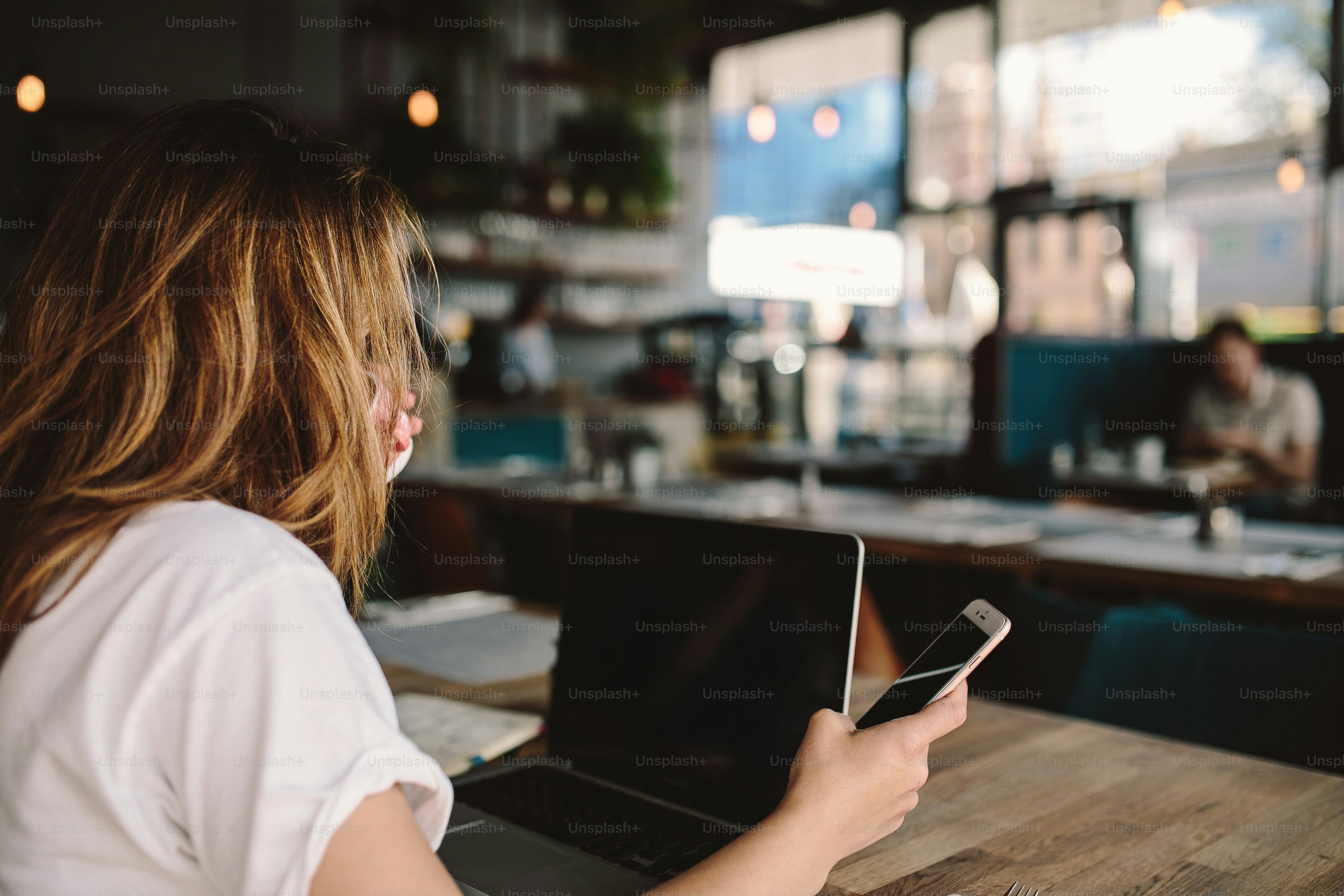 Wanita menggunakan ponsel dan laptop di kafe