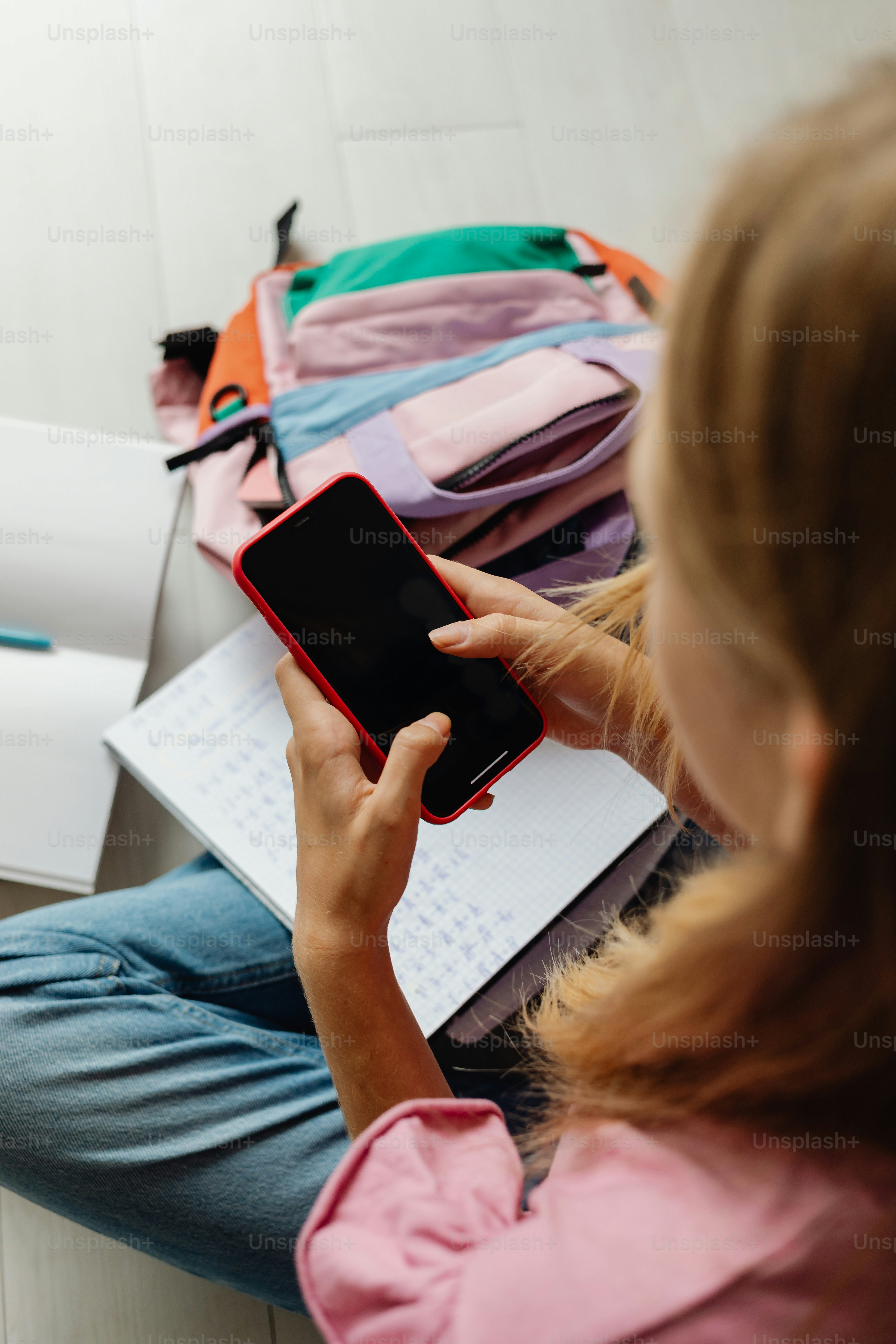 Gadis menggunakan smartphone dengan ransel dan buku