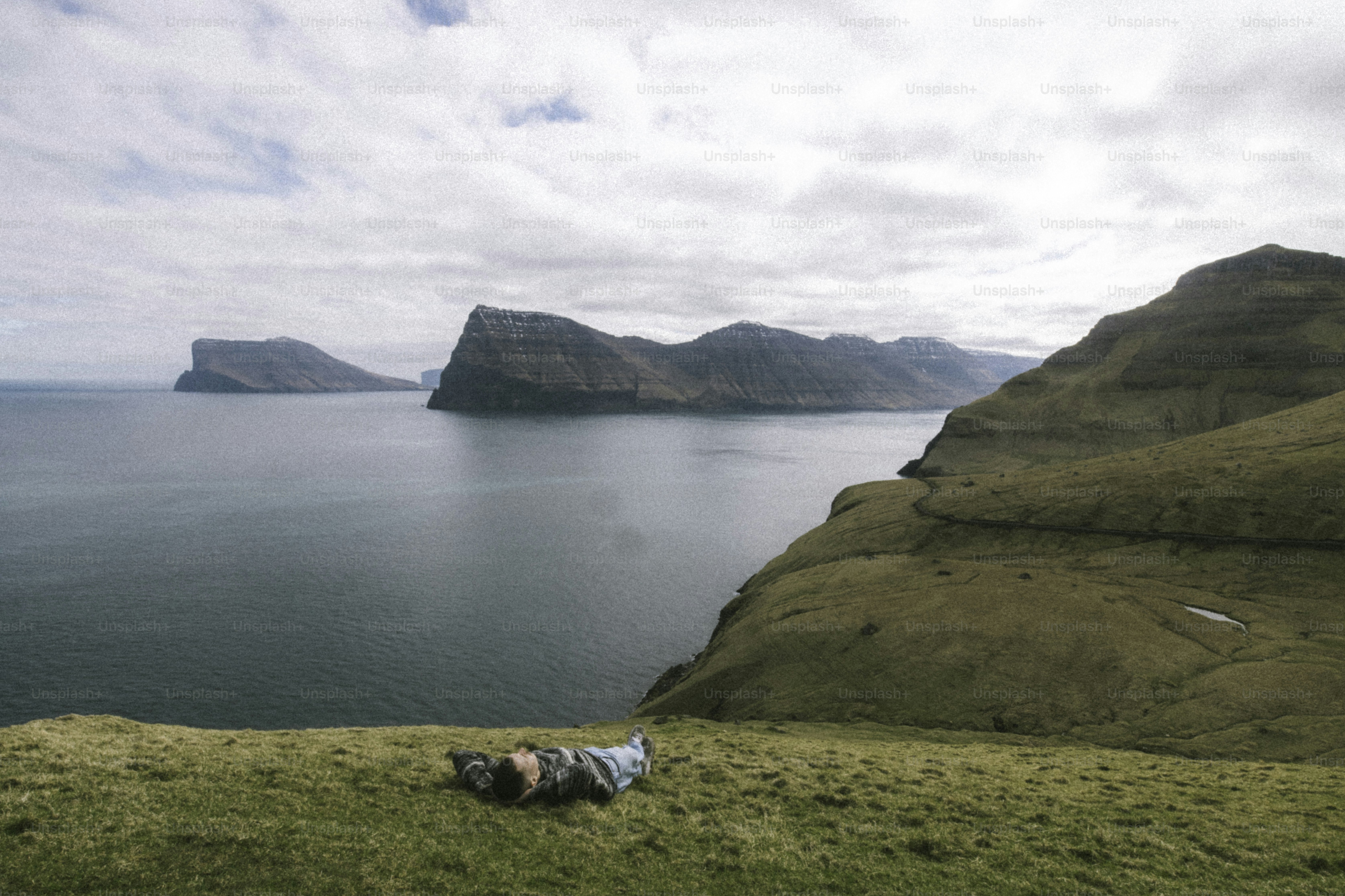 Person relaxing on grassy cliff overlooking ocean and islands