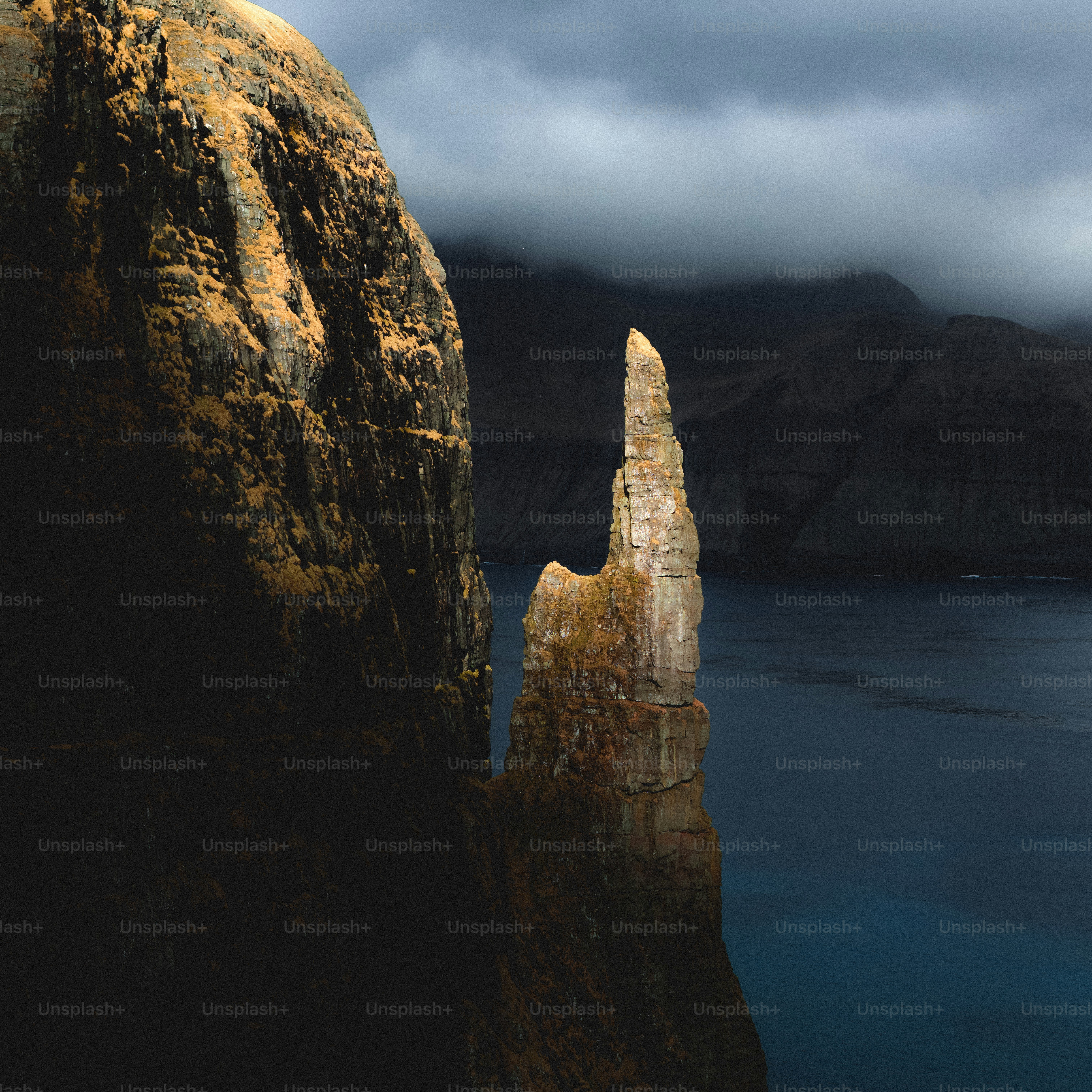 Jagged rock spire rises from the sea under cloudy skies