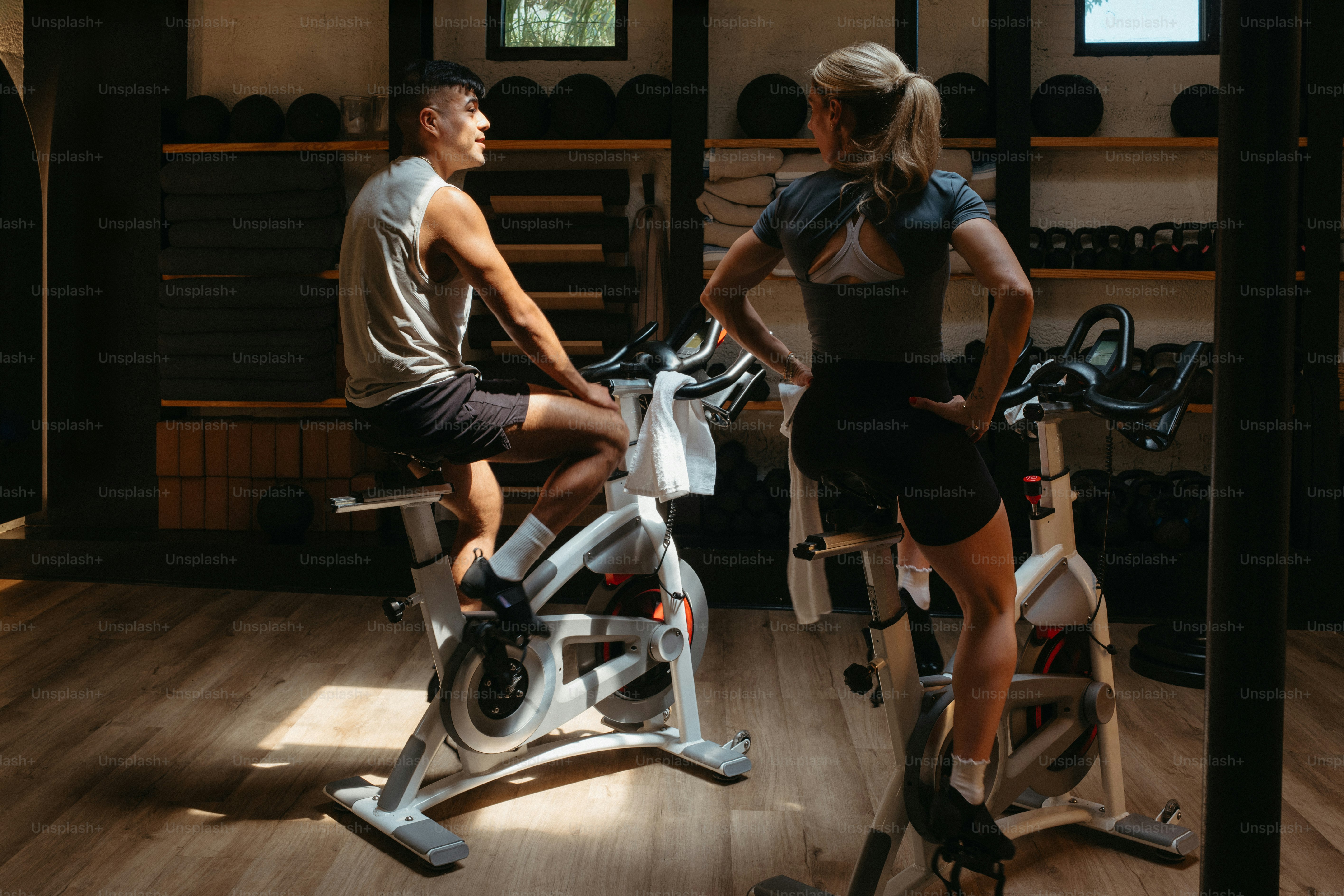 Zwei Personen, die auf Heimtrainern in einem Fitnessstudio Fahrrad fahren