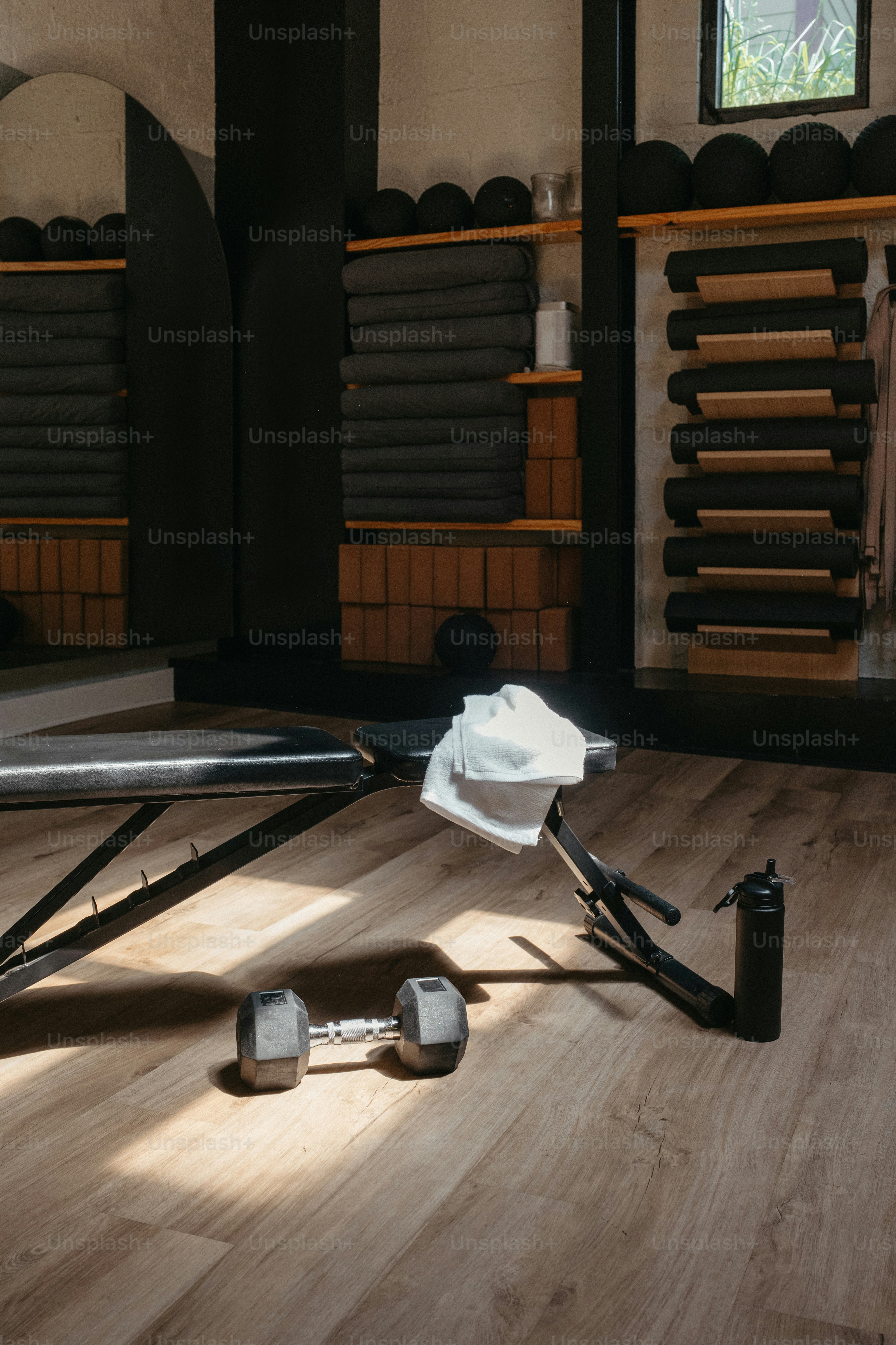 Dumbbell and water bottle on gym floor with bench.