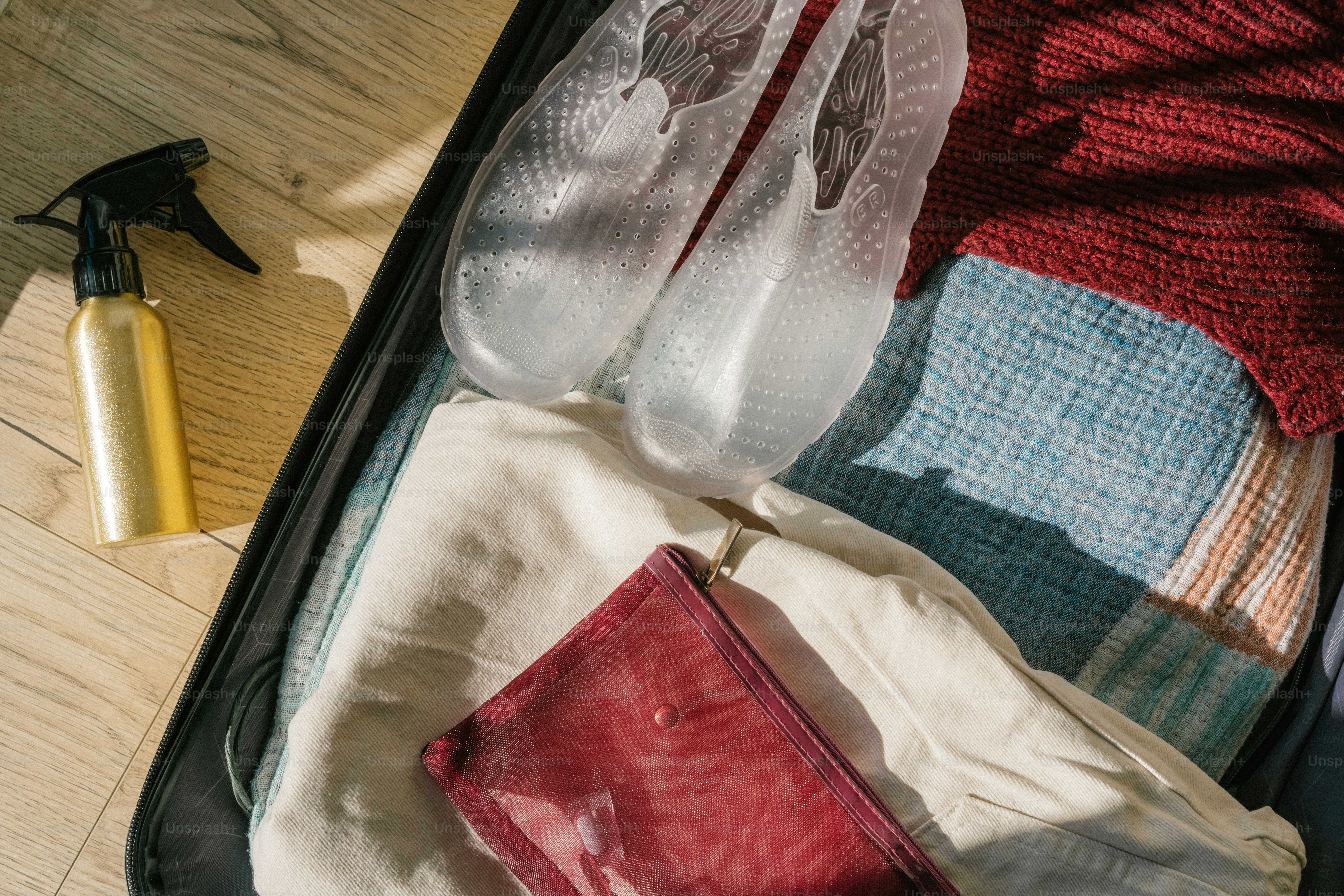 Suitcase packed with clothes, shoes, and spray bottle.