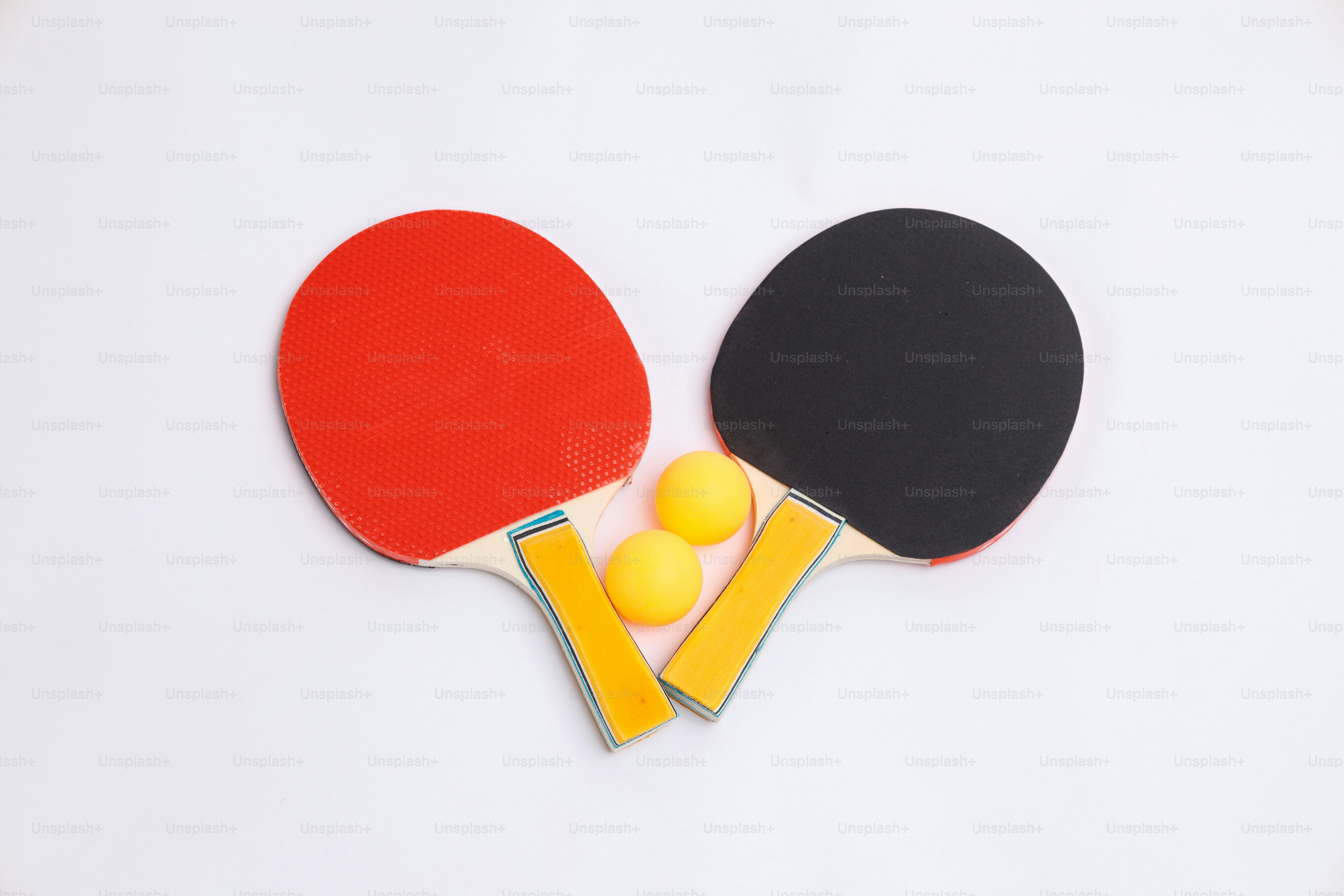 Two ping pong paddles and three balls on white.