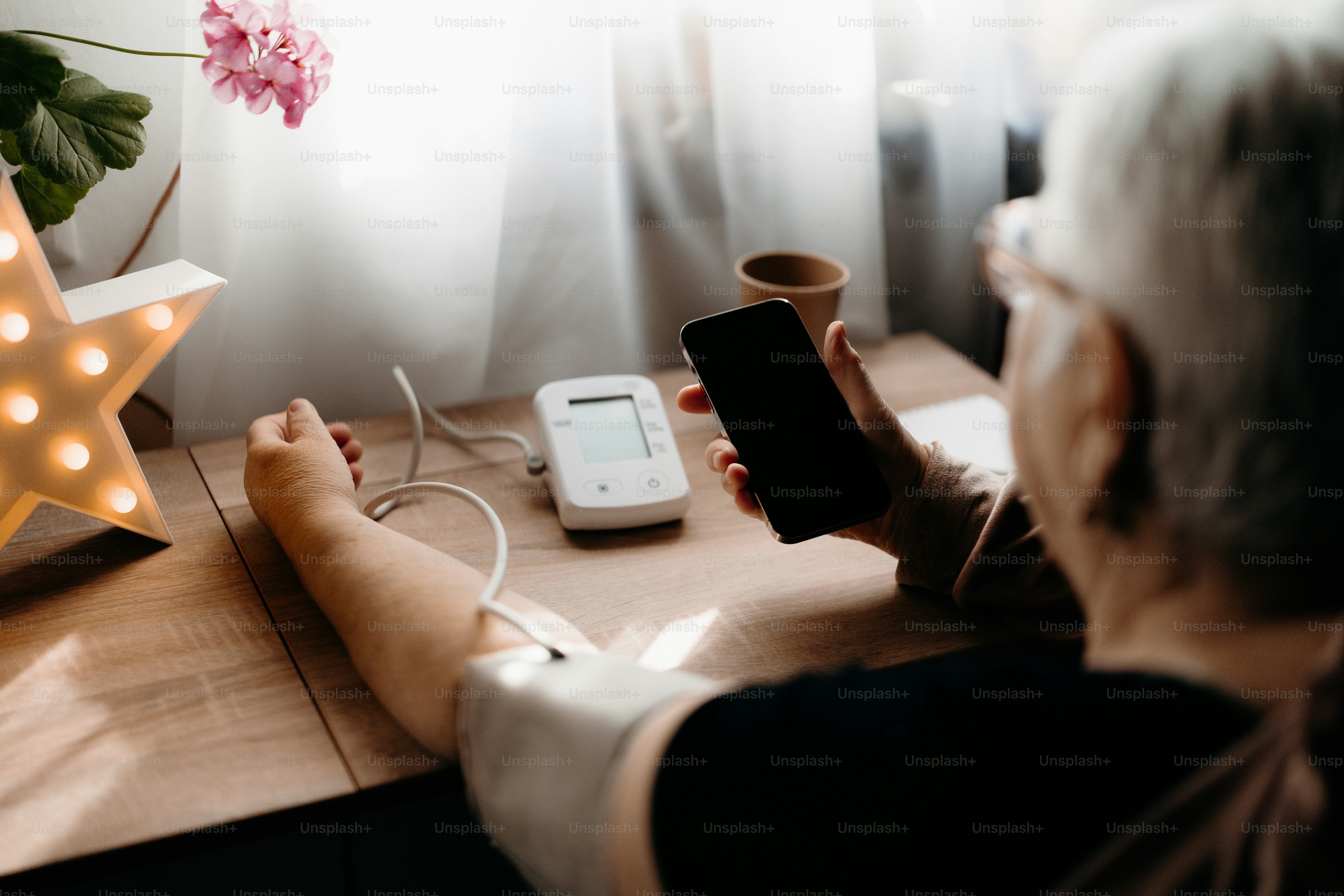 Ältere Person benutzt ein Blutdruckmessgerät und ein Smartphone.