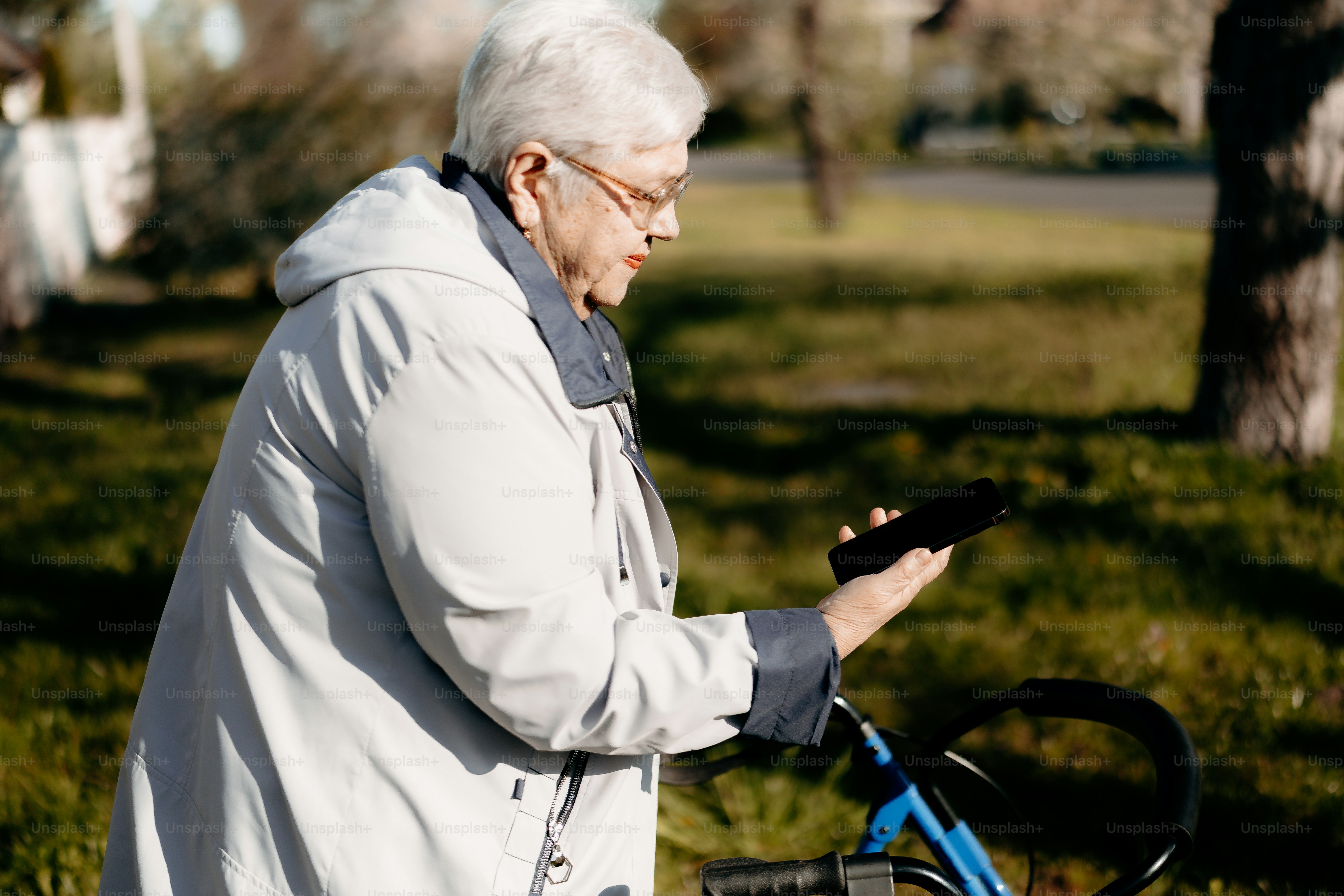 Eine ältere Frau mit einem Rollator schaut auf ihr Handy.